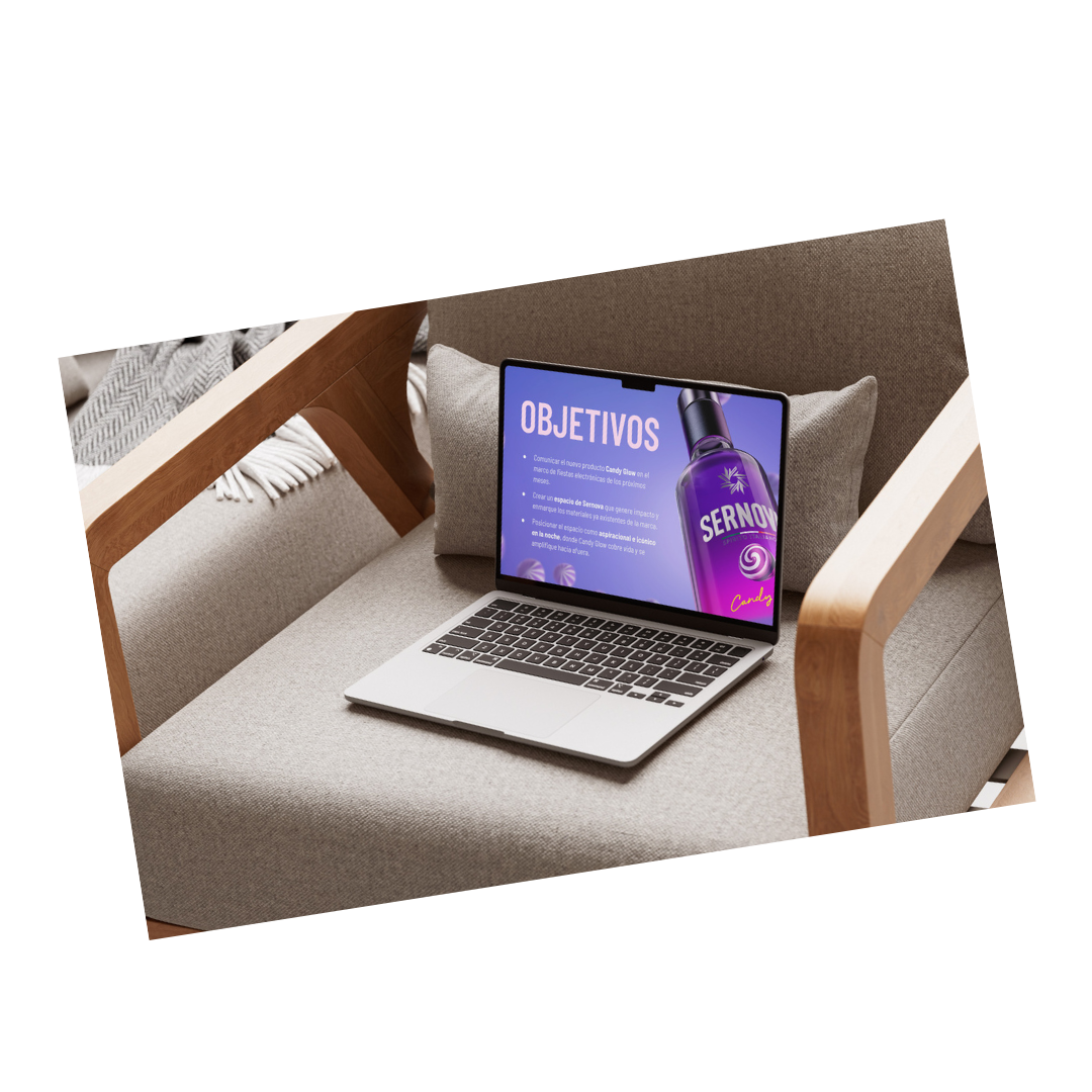 A laptop on a beige couch displaying a presentation with the heading 'OBJETIVOS' and an image of a purple bottle labeled 'SERNOY'.