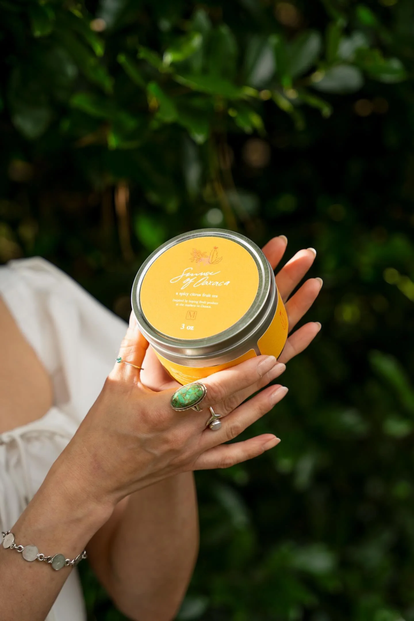 A person holding a yellow container of organic eye cream outdoors with greenery in the background.