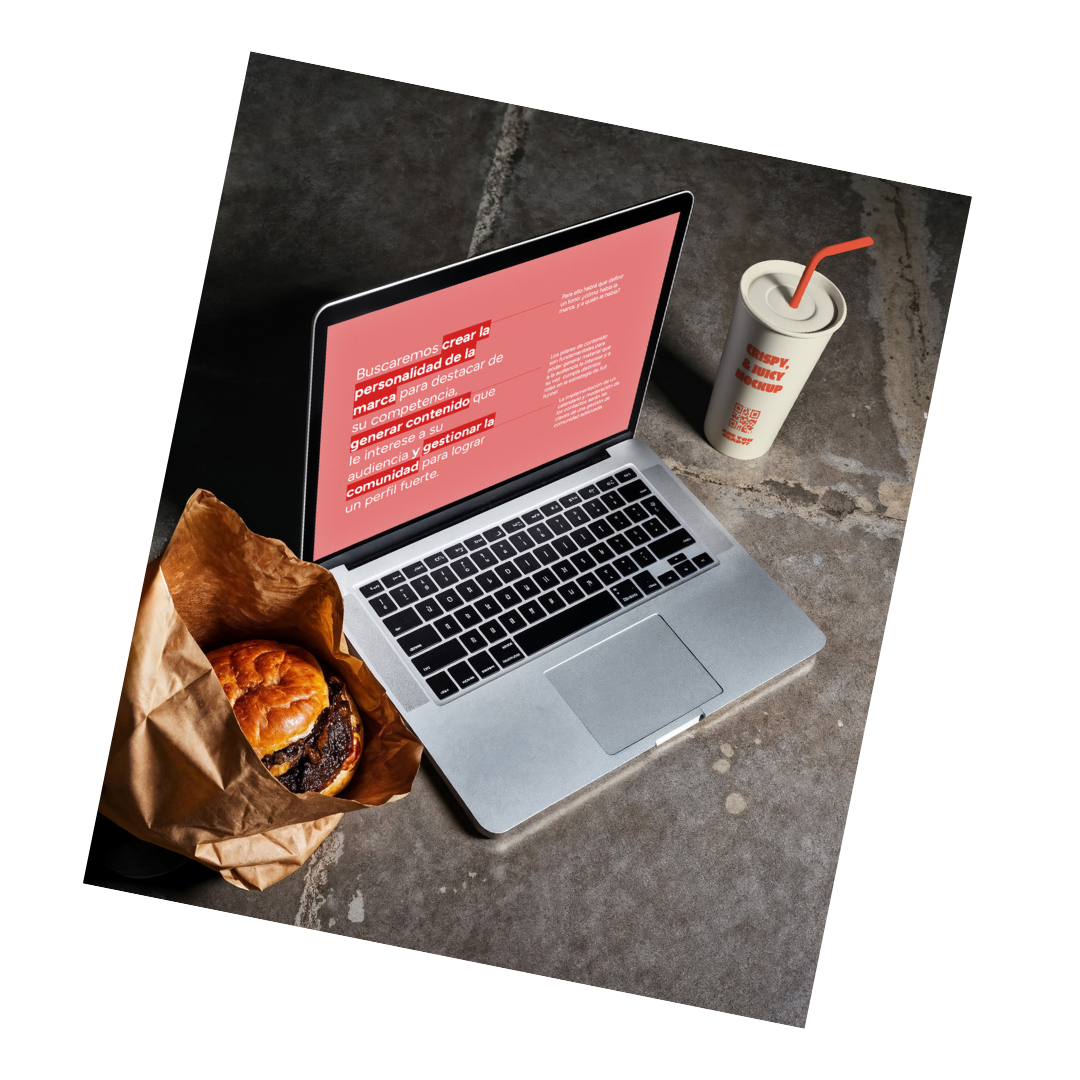 A laptop displaying a red screen with white text, a paper bag with a burger, and a soft drink with a straw on a concrete surface.