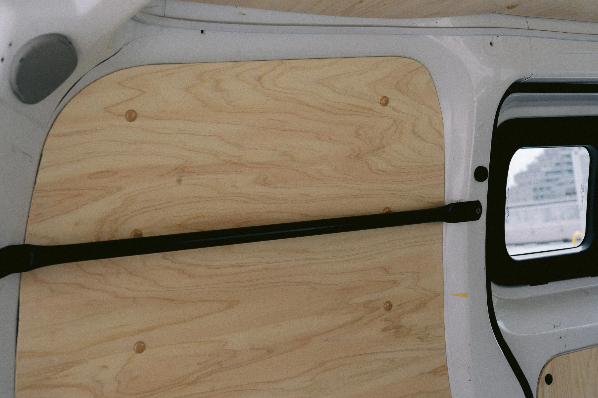 木製の板が取り付けられた車内の壁と窓。黒い棒が垂直に設置されている。