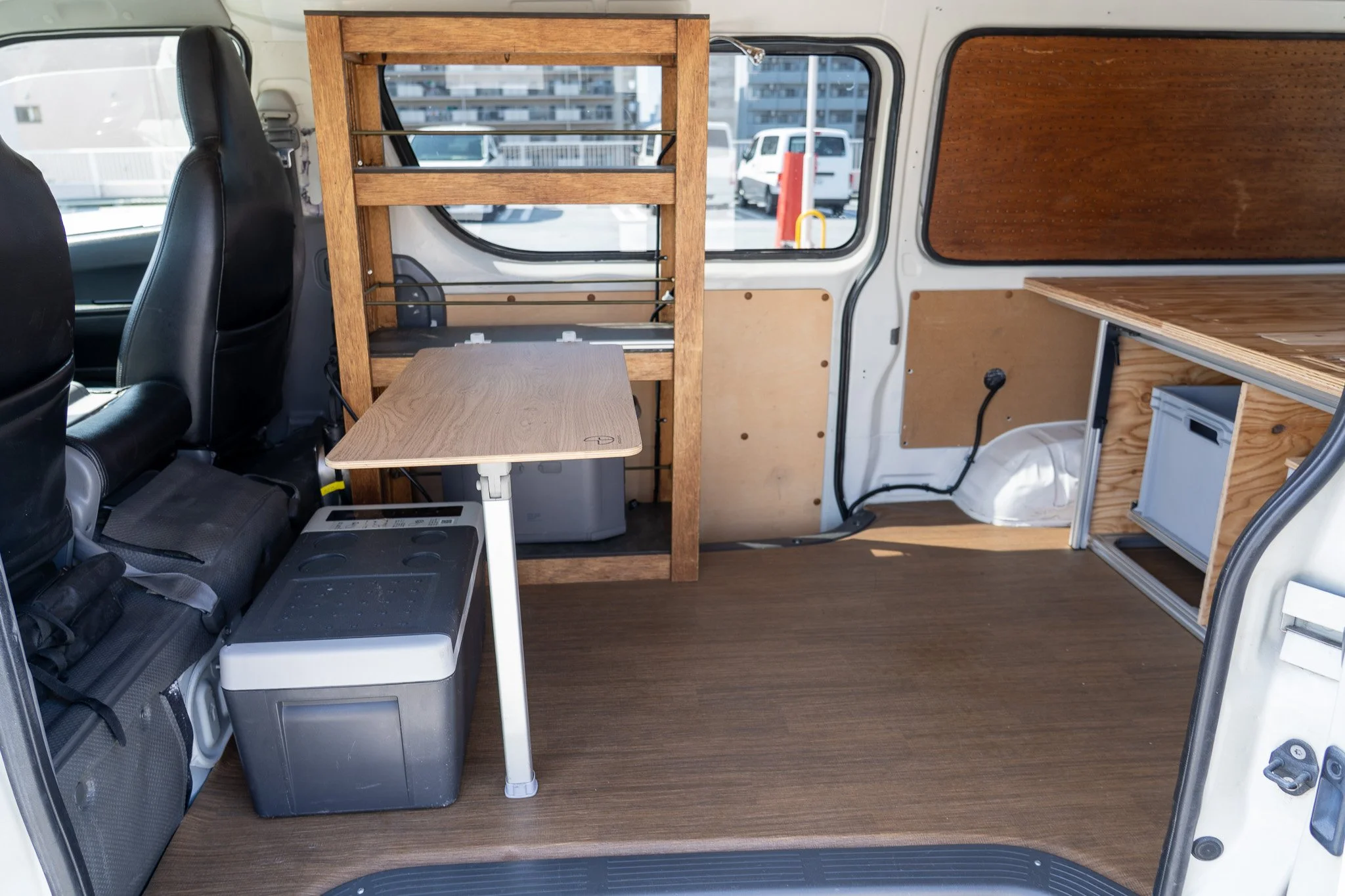 白いバンの内部、木製の棚と机、コンテナボックス。