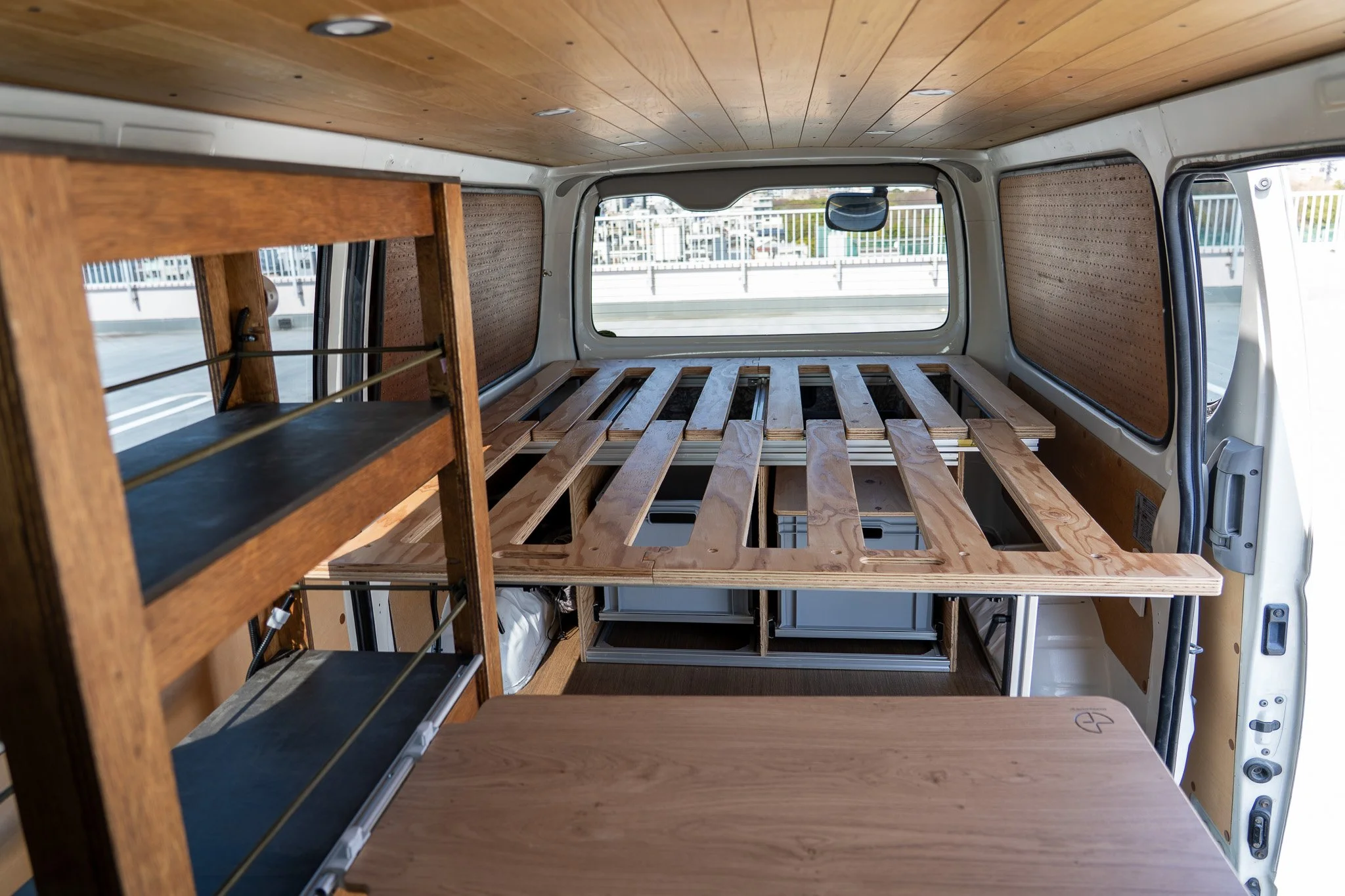 木製の棚とベッドフレームが車内に設置されたキャンピングカーの内部