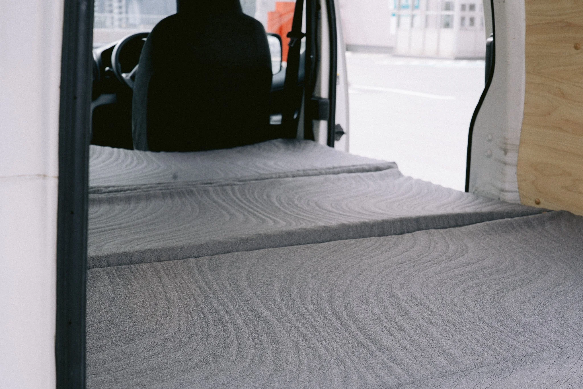 車の荷台に敷かれたグレーのカーペットと、運転席に乗る人物のシルエットが見える。