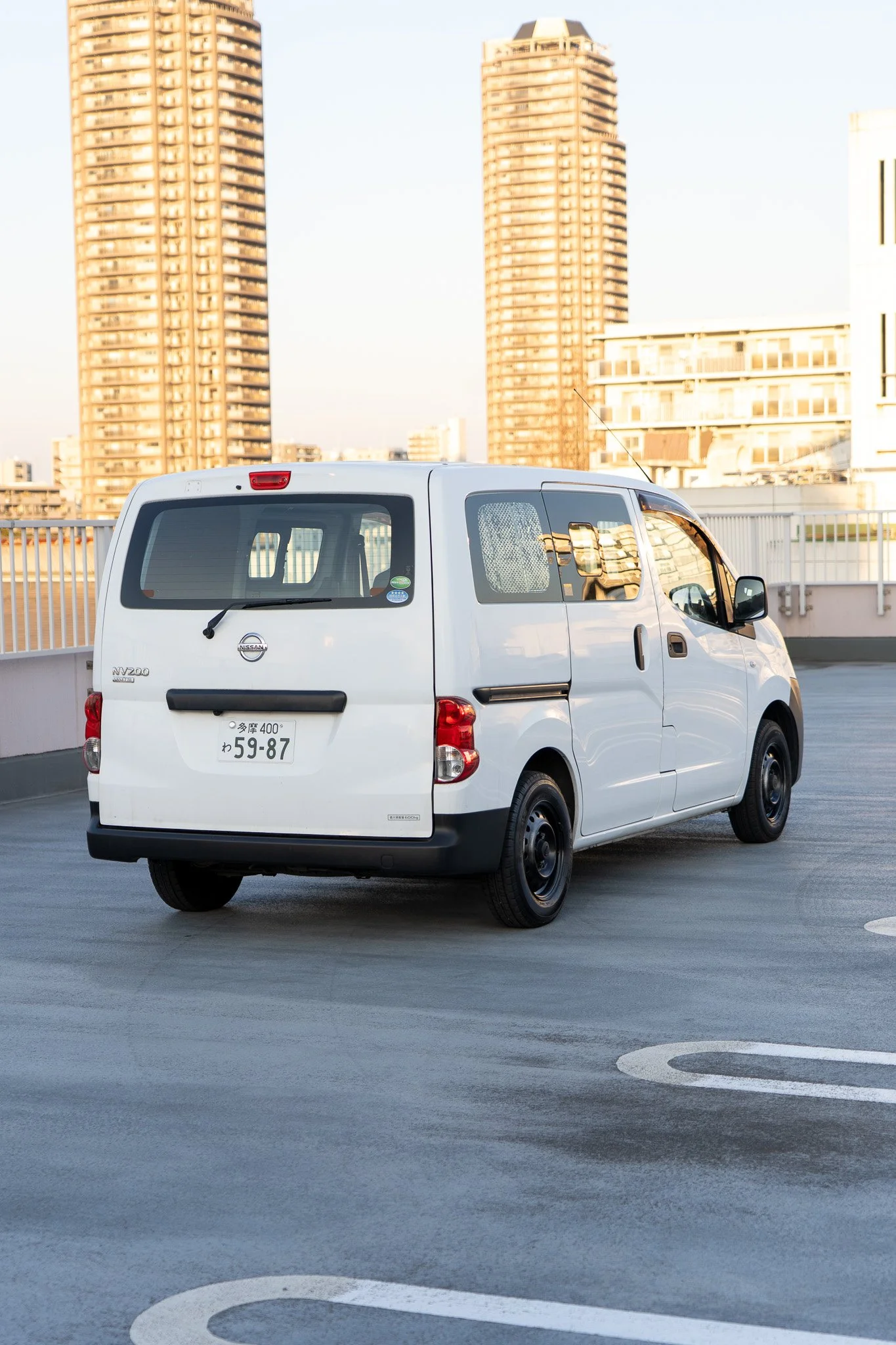 白色のバンが駐車されている都市の屋上駐車場と高層ビル群の背景