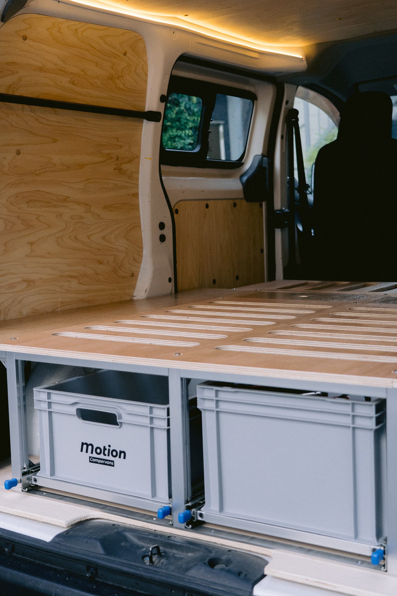 キャンピングカーの車内の改装された荷台部分の写真。木製の床と仕切り壁が設置され、収納用のボックスが見える。