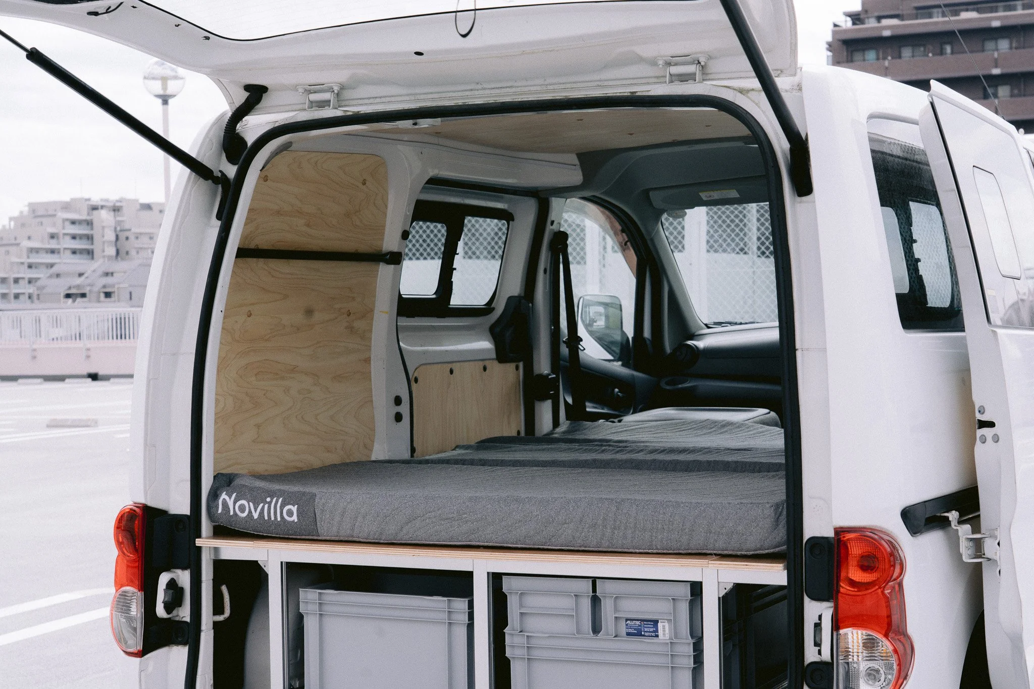 荷台が改造された白いバンの内部、木製の仕切りとベッドスペースがある