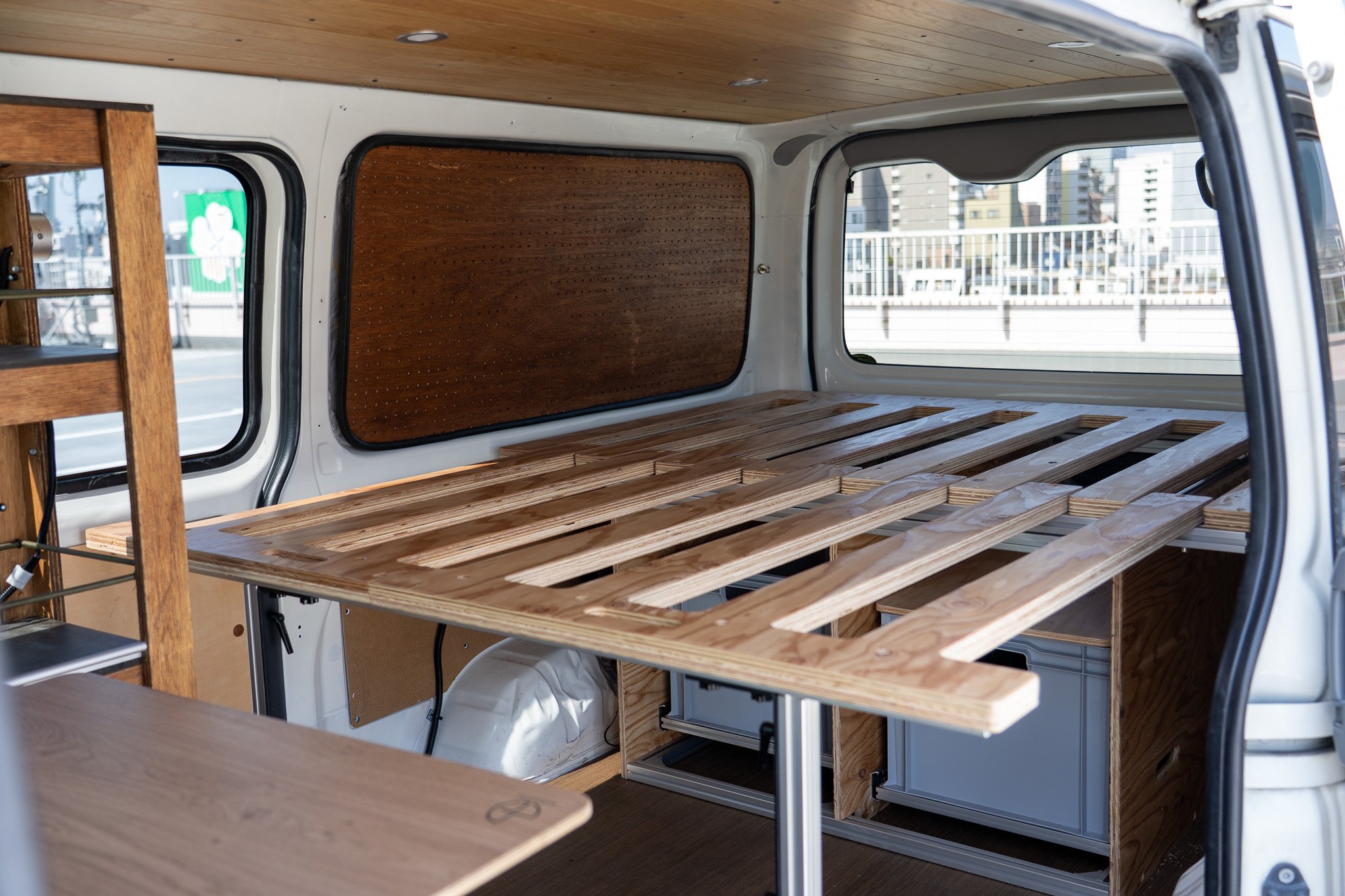 木製の棚とテーブルが設置されたバンの内部、窓から都市の風景が見える