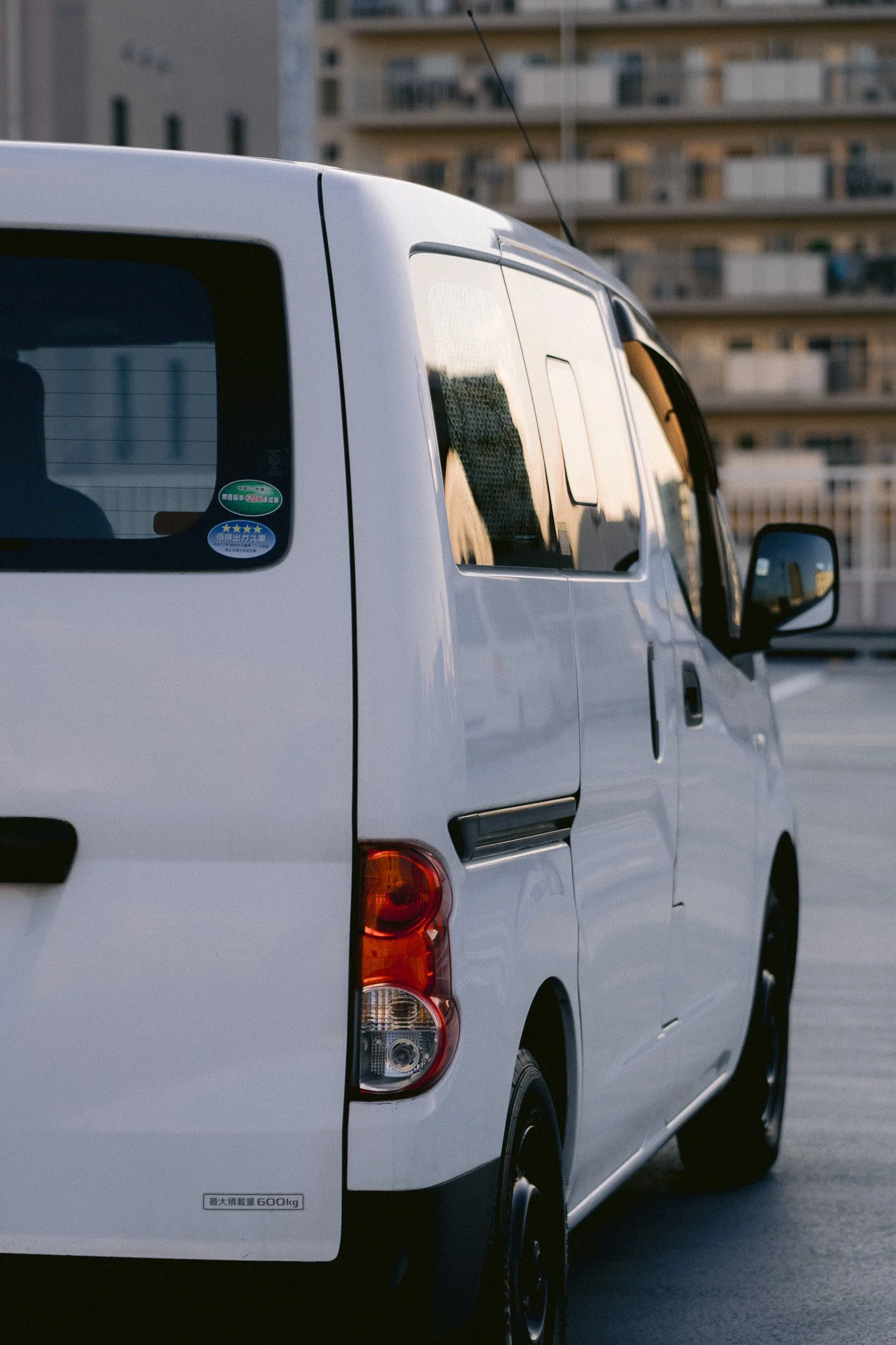 白色の軽トラック車両が都市の高層マンションの背景に停車している。