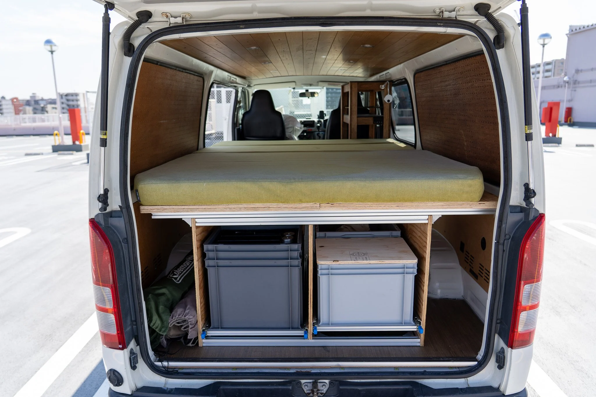 Campervan rear storage with double bed platform and organized storage boxes underneath