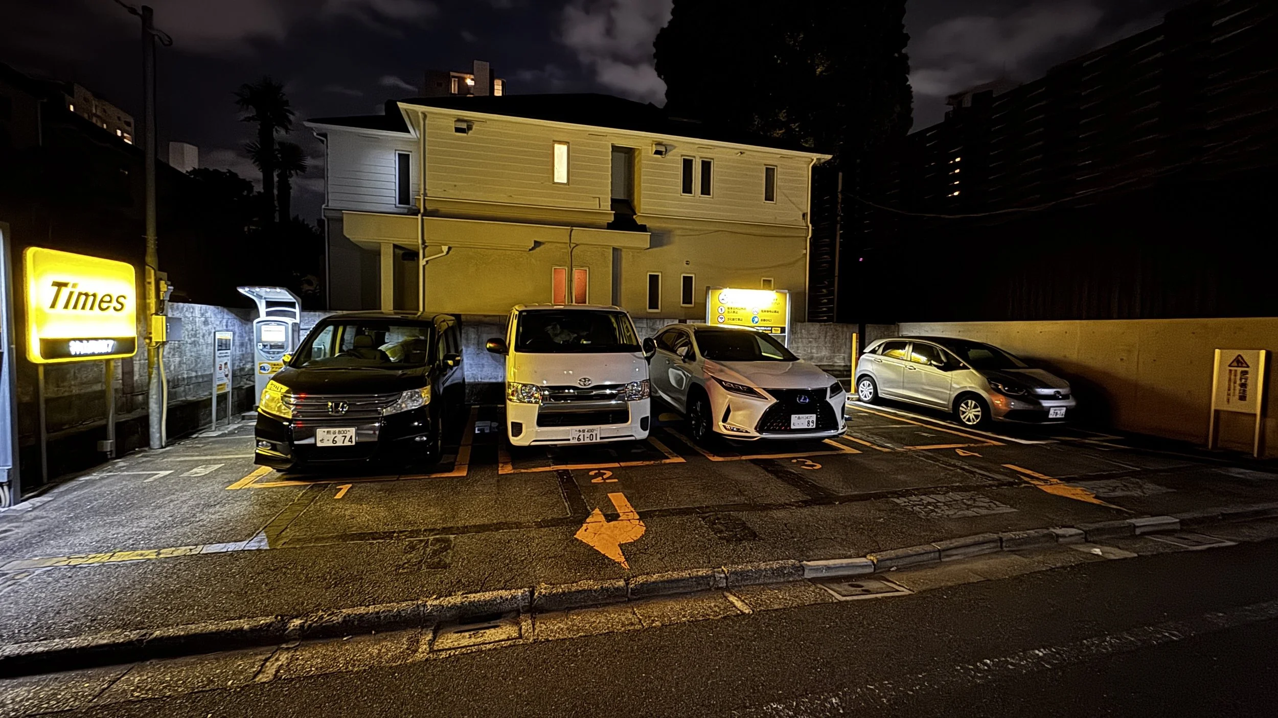 Campervan parked between cars in quiet Tokyo Times coin parking with house rules sign