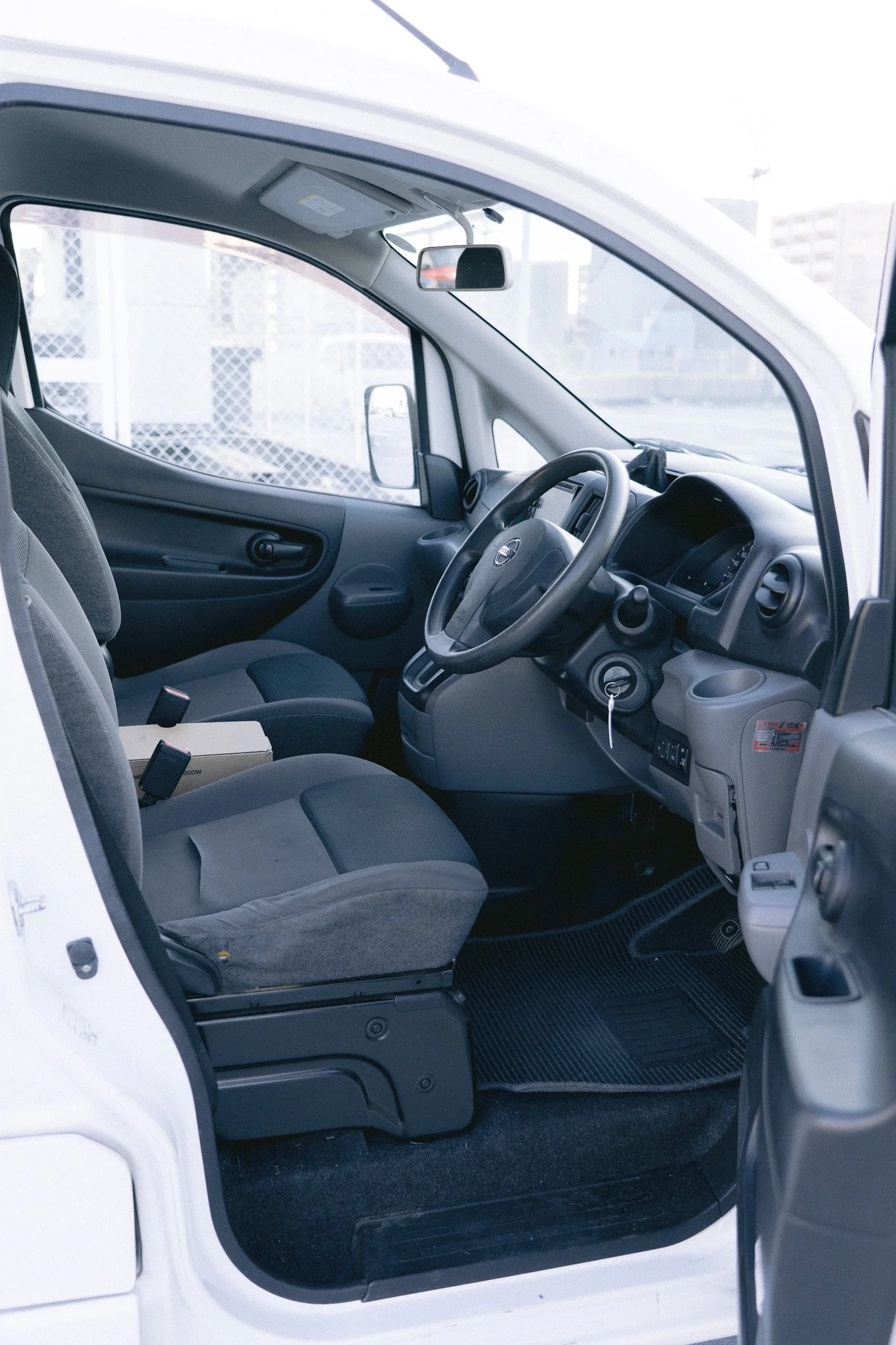 運転席と助手席の内装、メーターとステアリングホイール、座席には少し汚れと箱が置かれている。