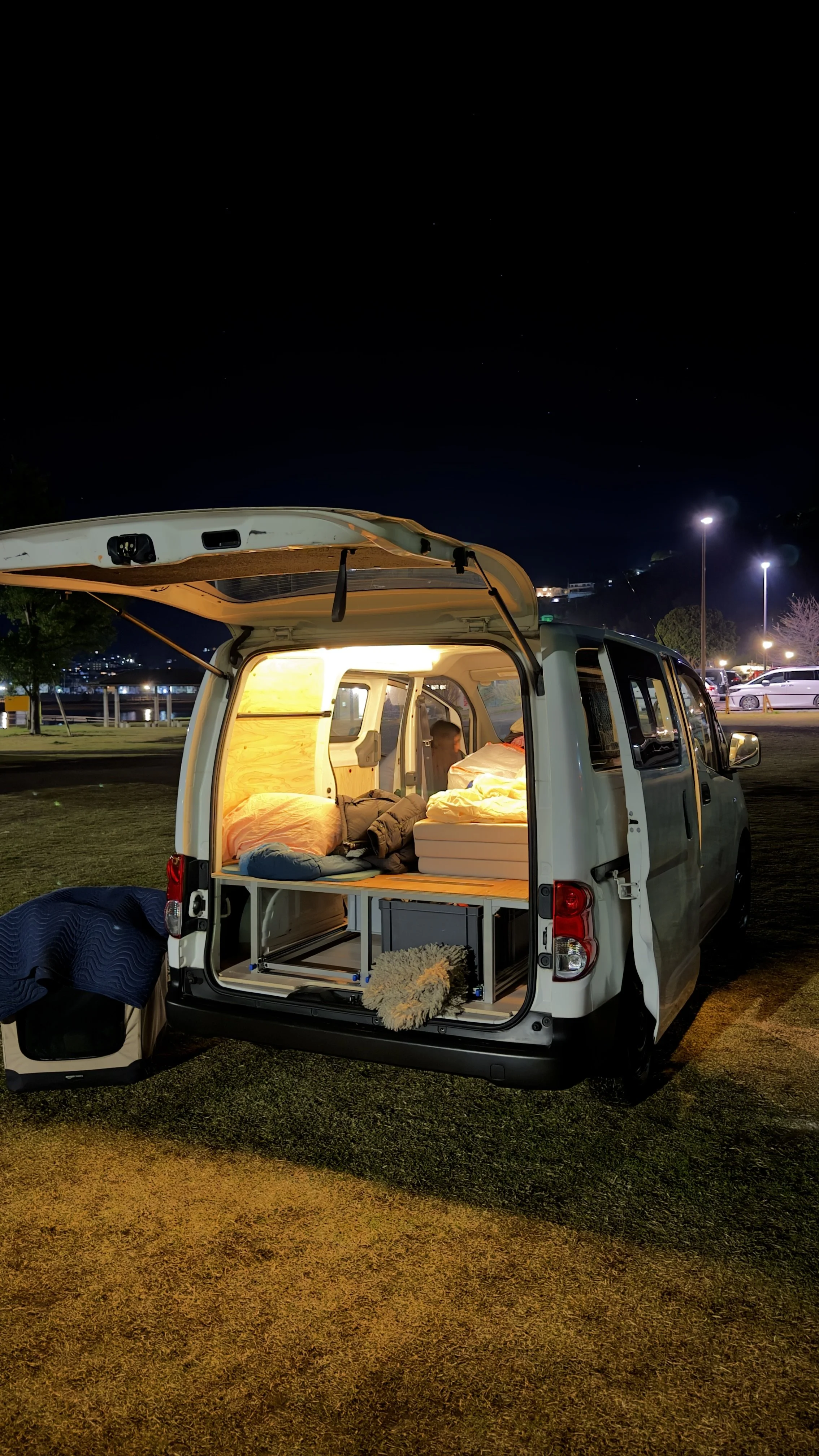 Sleeping in a campervan at night by a river in Japan, rear hatch open with the bed lit up