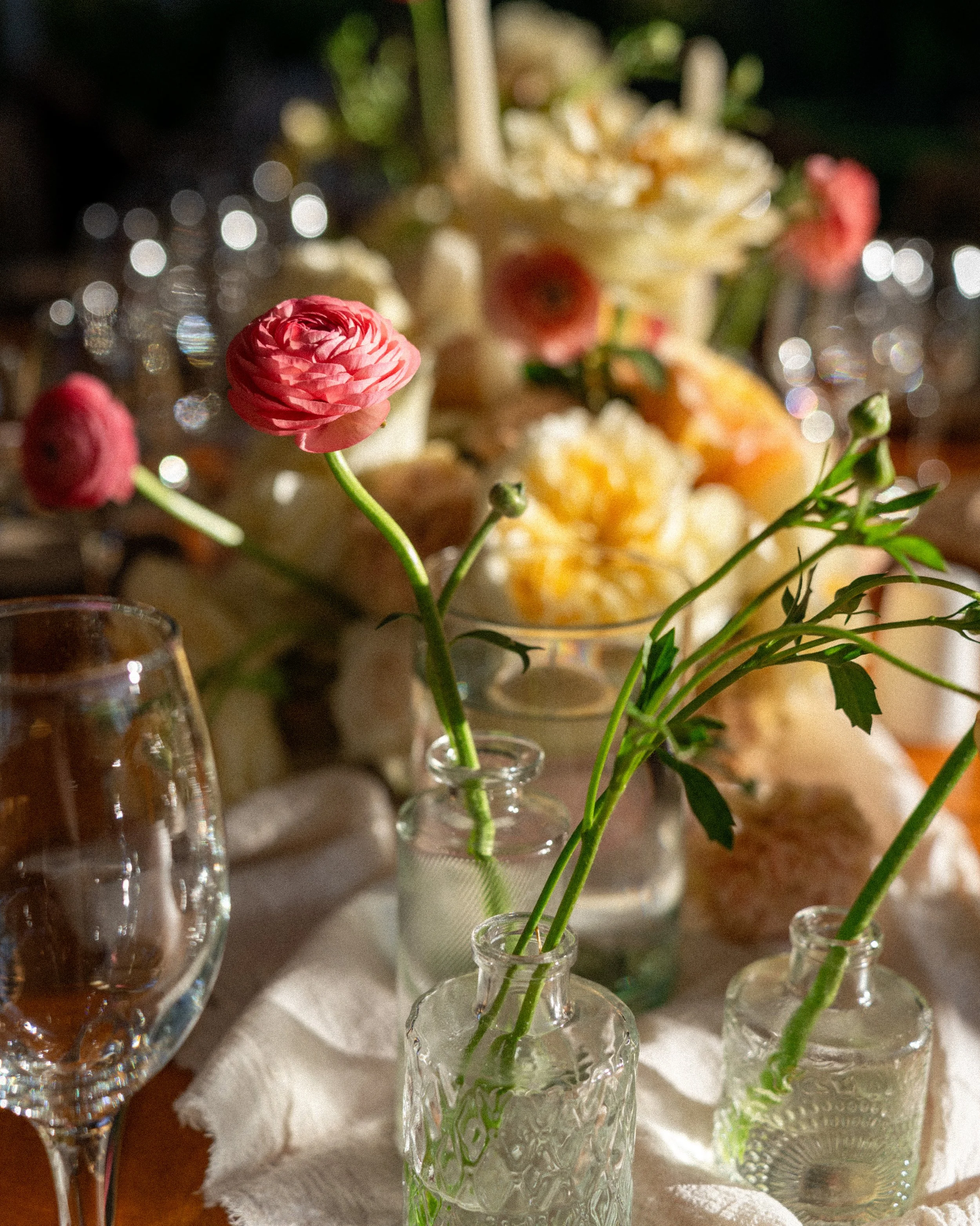 Vasos con flores en una mesa decorada para una celebración, con platos y copas de vino. Boda Ale y Robby, Bautizo Carlota, arreglos florales por DAGA Studio