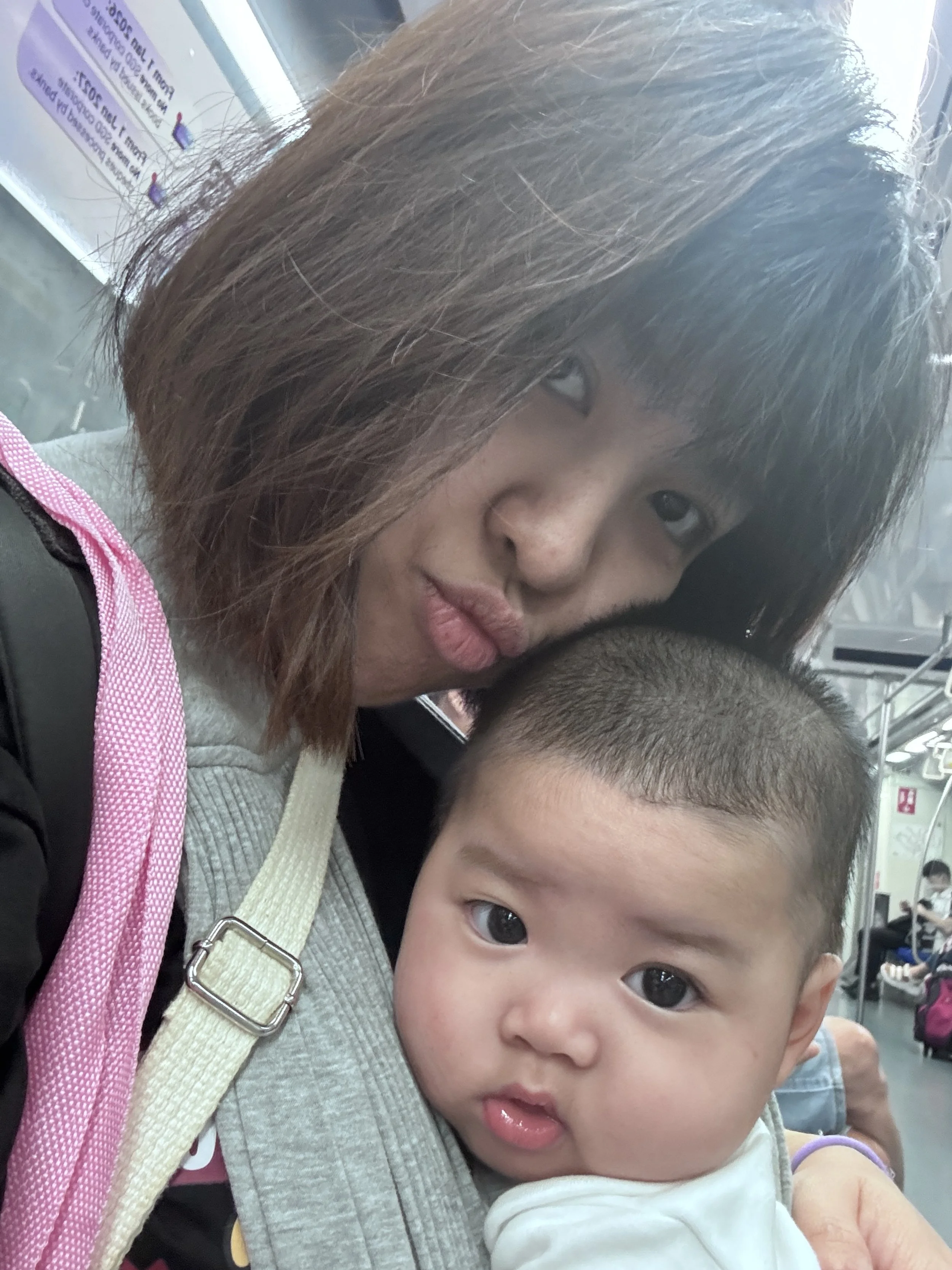 A young woman hugging a small child on a train, with other passengers seated in the background.