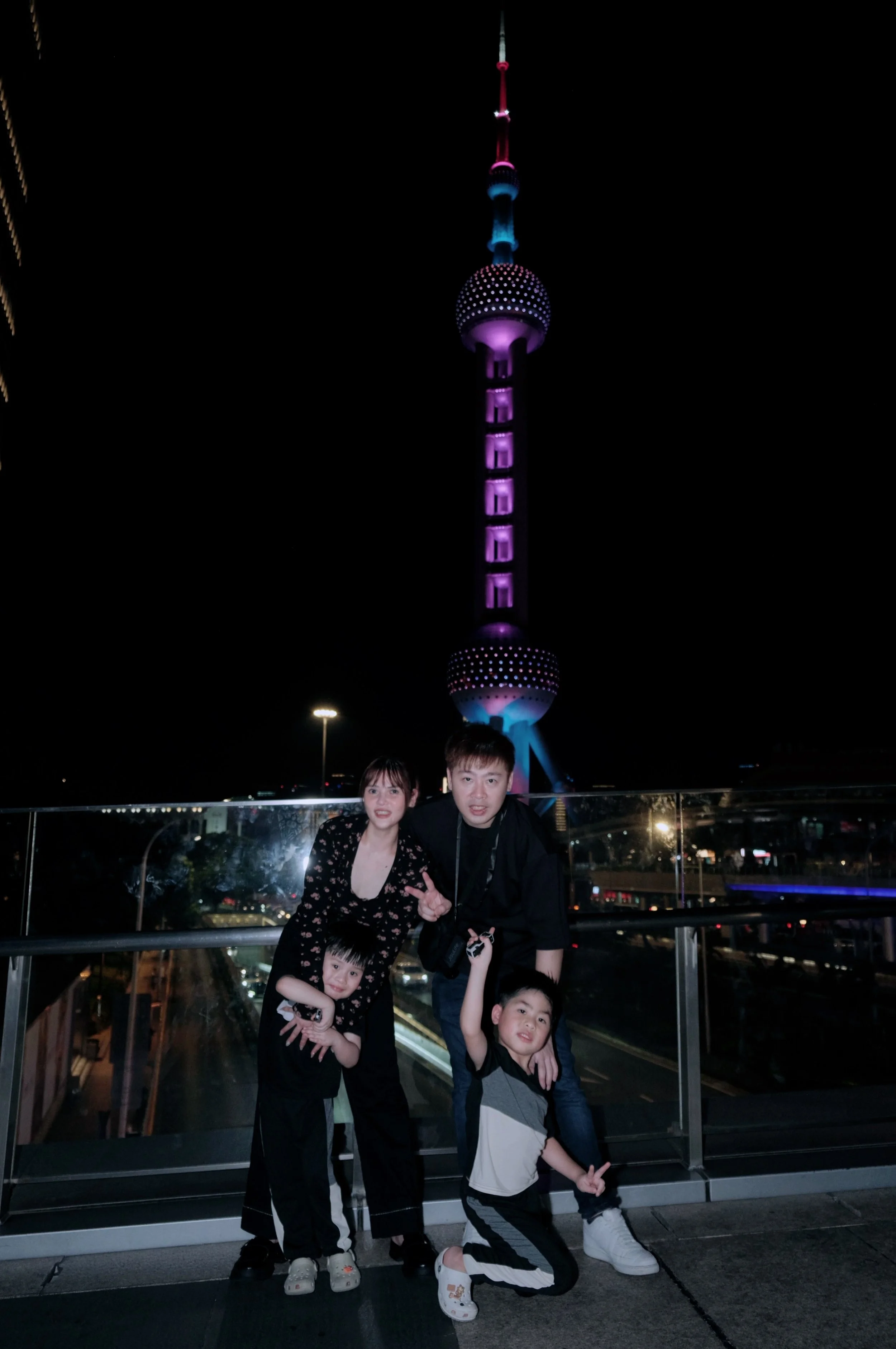 A family of four standing on a rooftop at night with the illuminated Oriental Pearl Tower in Shanghai in the background.