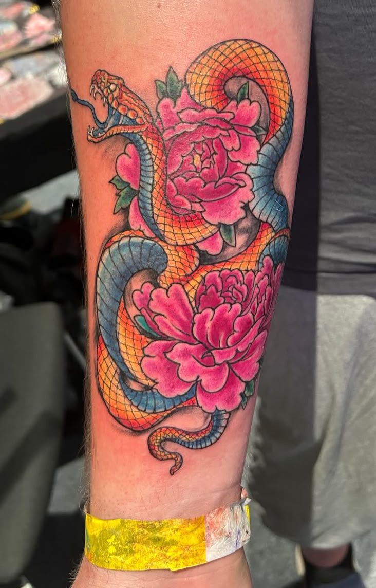 Colorful tattoo of a snake intertwined with pink peony flowers on a person's arm.