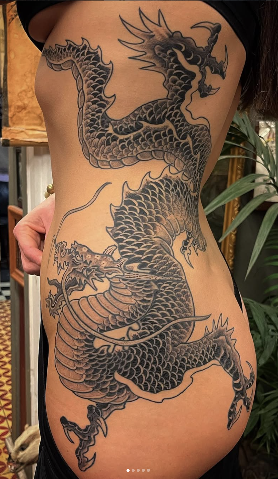 Black and gray dragon tattoo on person's torso with scales, claws, and fierce expression.