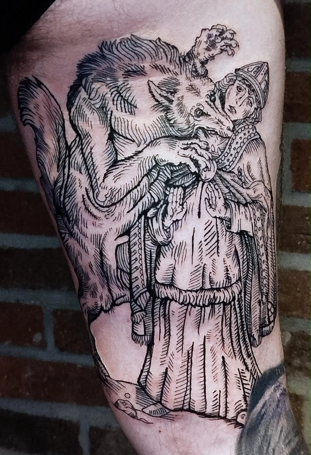 A black and white tattoo of the biblical story with a wolf, a young girl dressed in traditional robe, and a devil. The wolf appears to be twisting around the girl, who is holding a ball. The design is detailed with fine lines and shading.