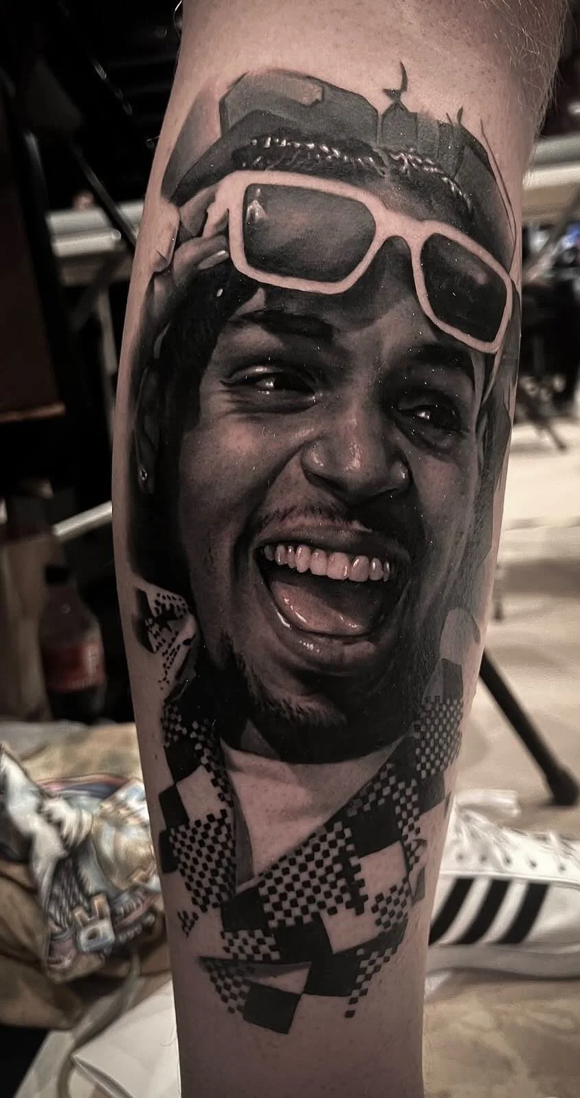 Black and gray realistic tattoo of a woman laughing with sunglasses on her head, with additional geometric and abstract design elements.