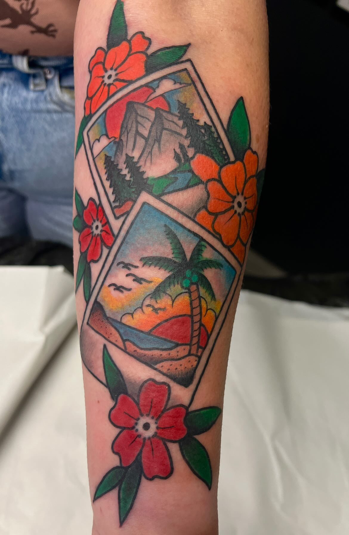 Colorful tattoo of tropical scenes, including a mountain, palm tree, ocean, sunset, and flowers.