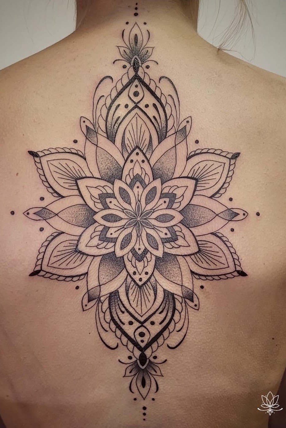 Black and grey geometric floral tattoo on a person's back with symmetrical intricate patterns resembling a lotus flower.