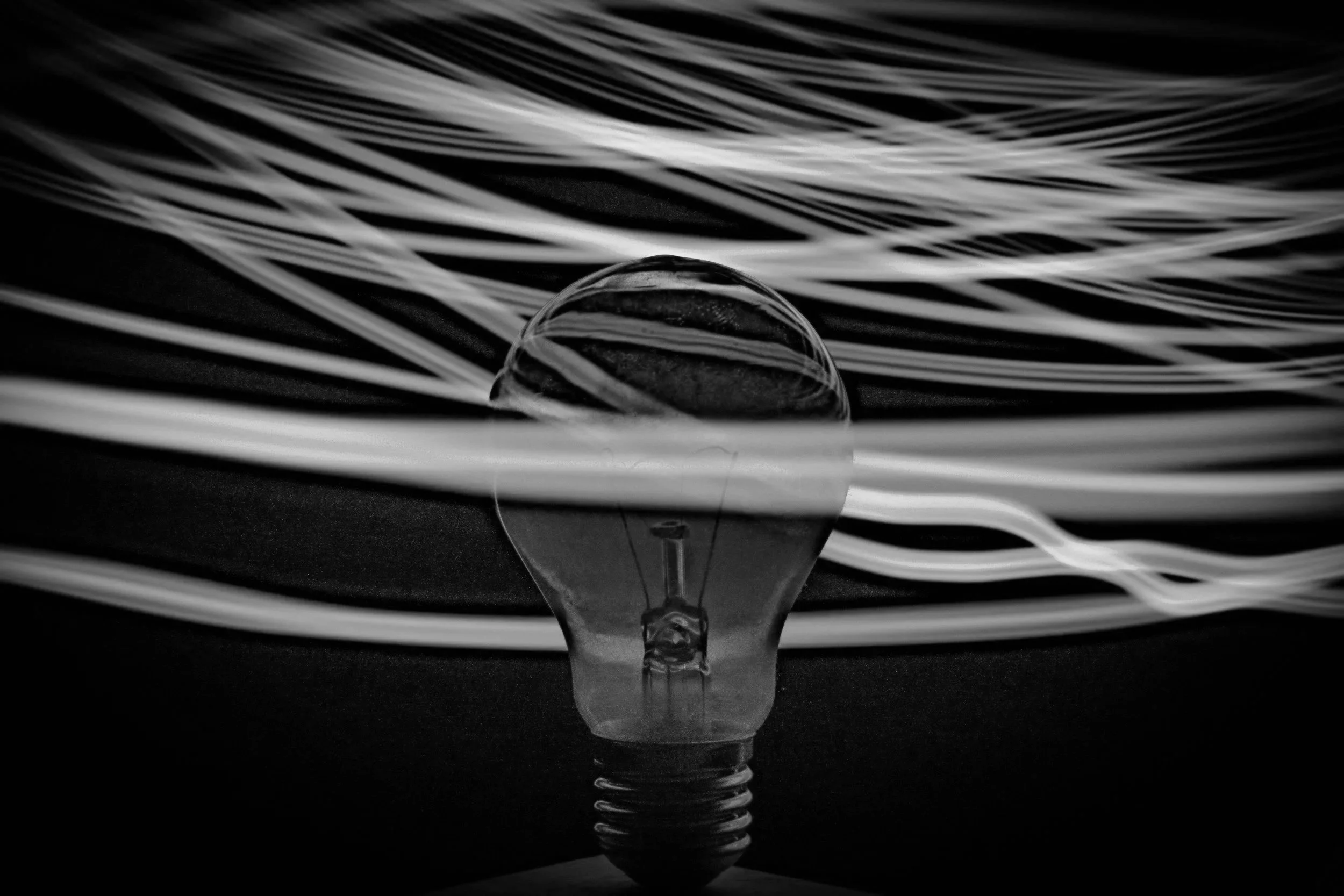 Close-up of a light bulb with swirling white optical fibers in the background.