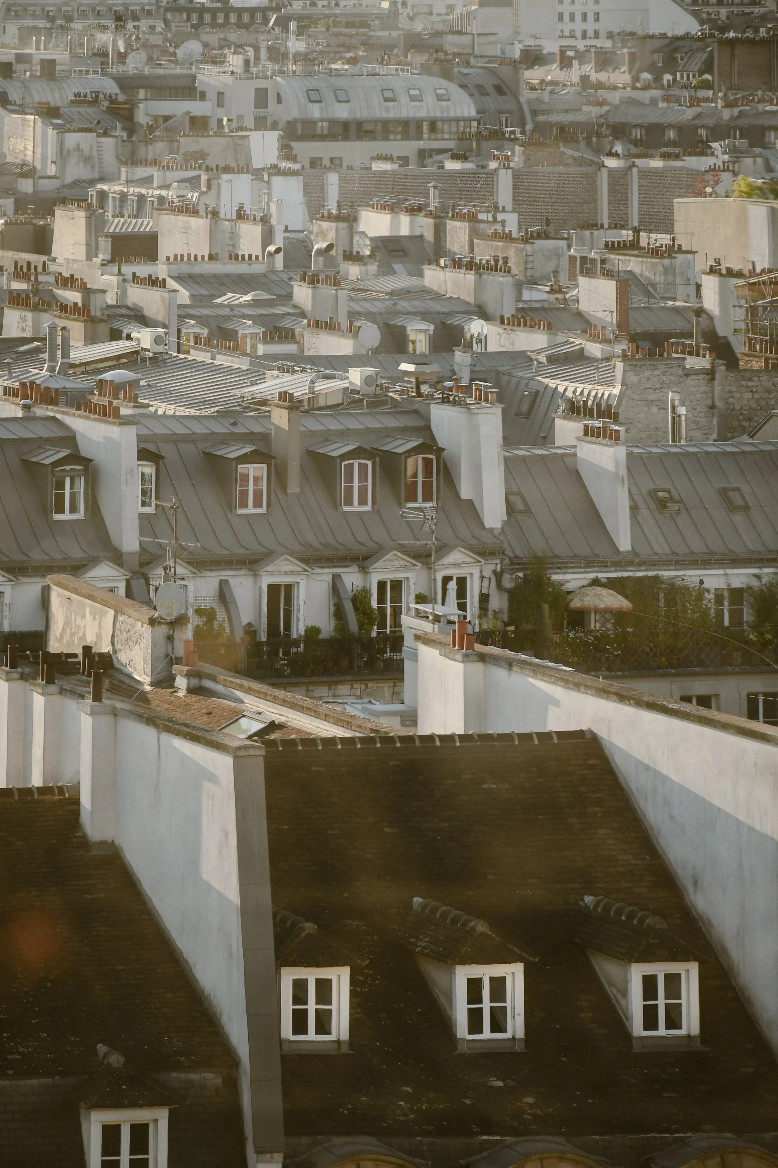 Vues rapprochées de toits de bâtiments résidentiels à Paris avec des cheminées, des fenêtres à volets, et des éléments d'urbanisme comme des antennes et des cintres.