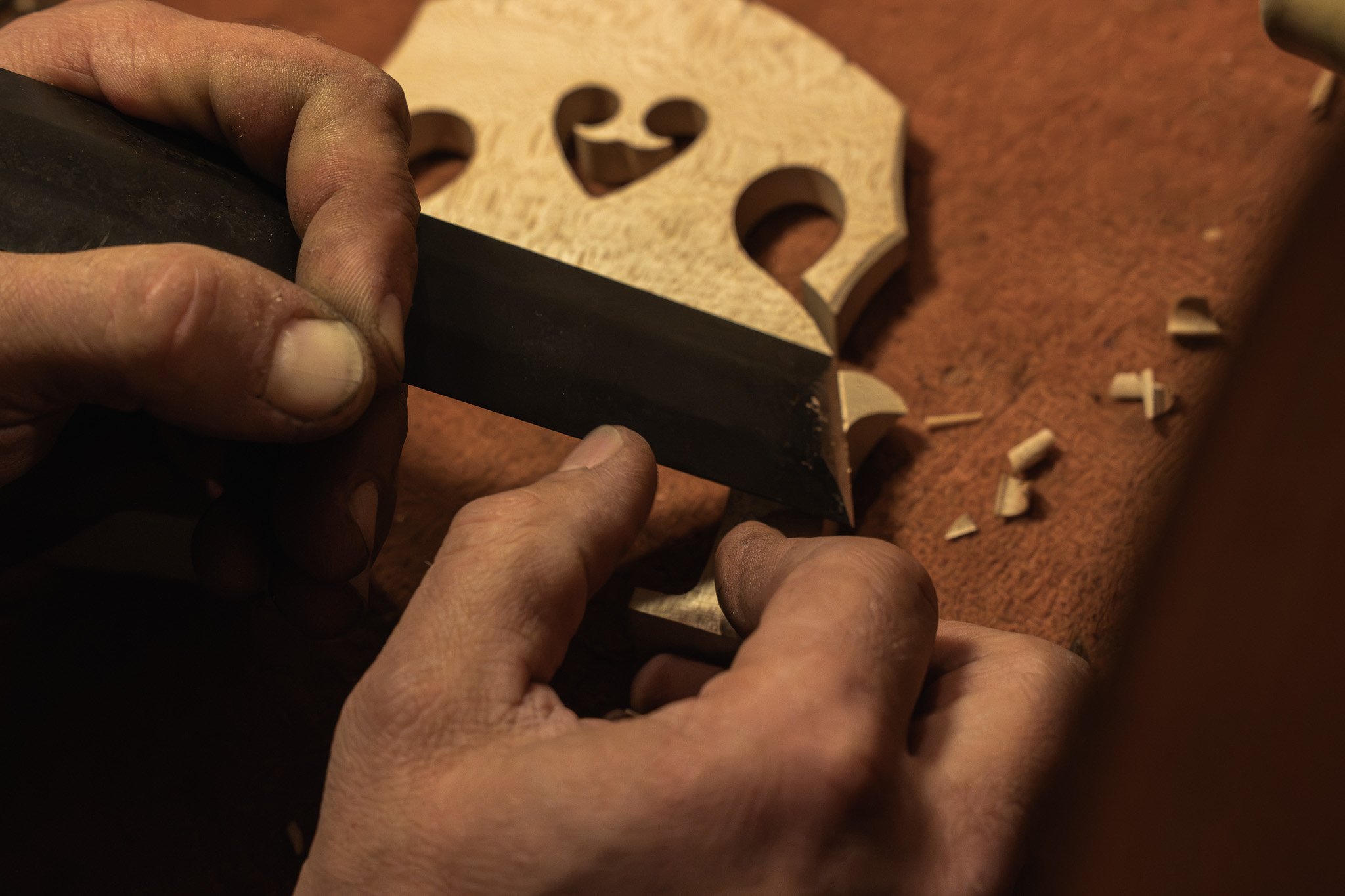 Handen die een stuk hout bewerken met een mes, terwijl er snippers hout op een tafel liggen.