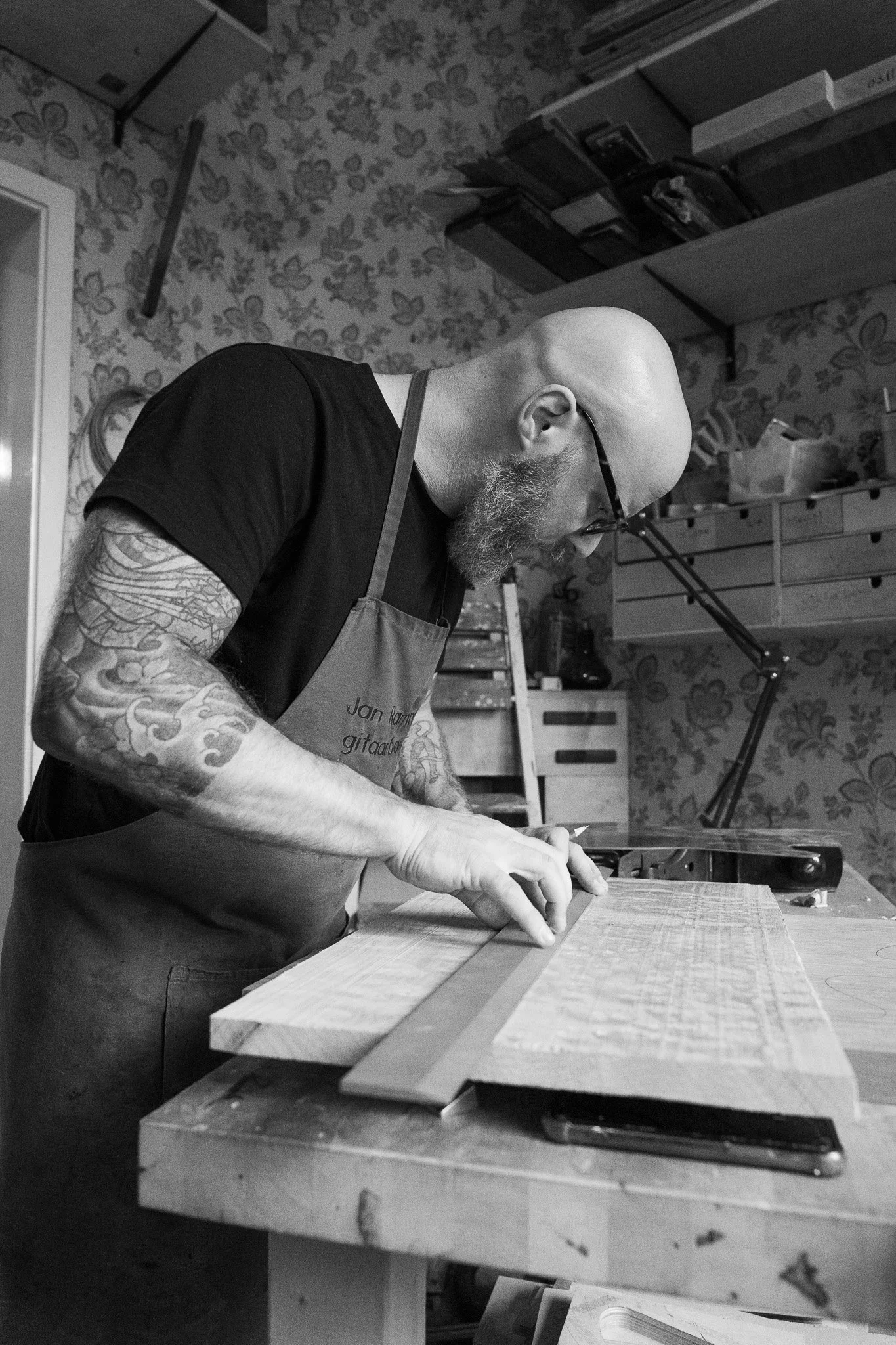 een luthier staat in zijn werkplaats in een custom shop en tekent een gitaar uit op hout