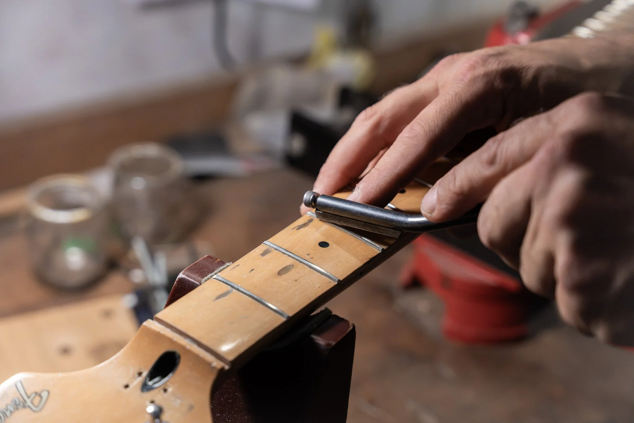 Een close-up van handen die een gitaar stemmen met een stemknop in een werkplaats of muzieklaboratorium.