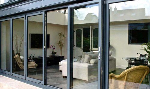 Living room viewed through glass sliding doors, with sofa, armchair, and plants.