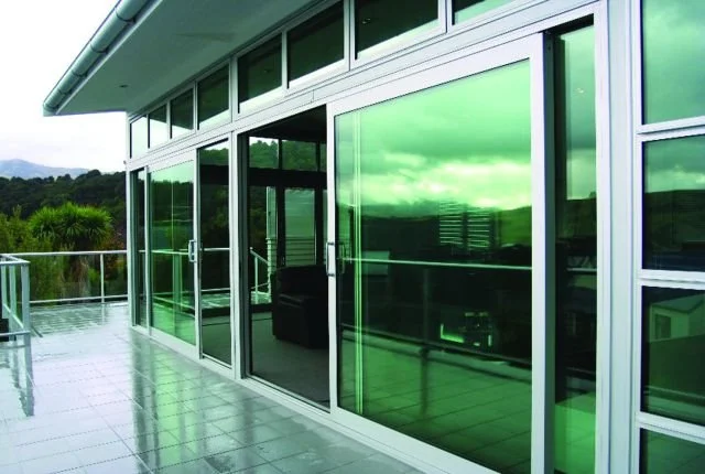 Modern balcony with glass sliding doors and green-tinted windows, overlooking a lush landscape.
