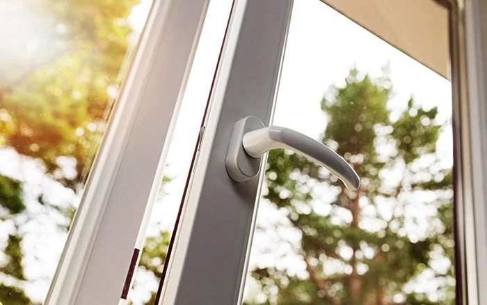 Close-up of a white door handle on a glass door with trees outside