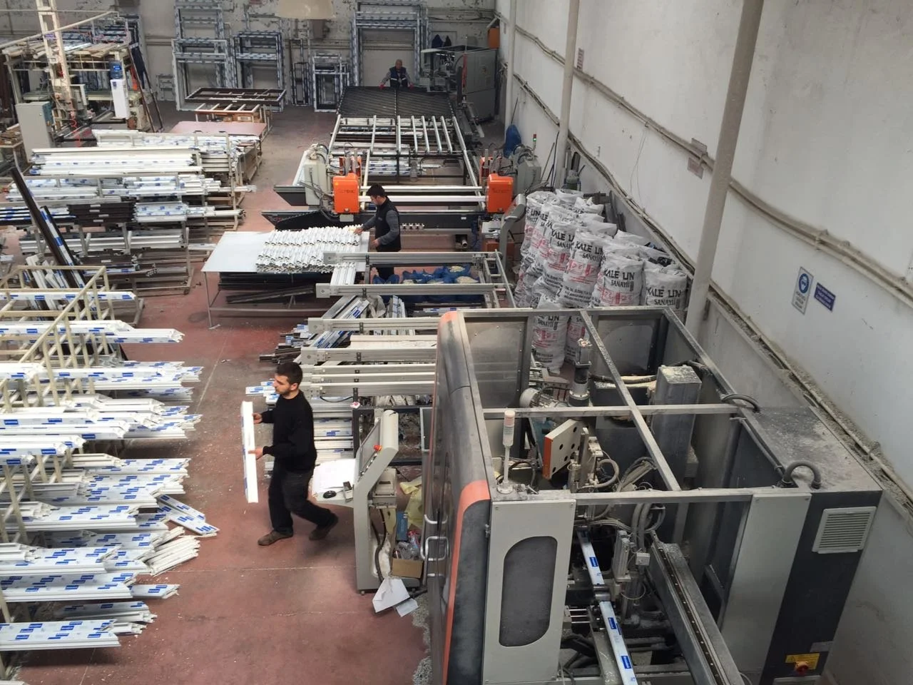 A manufacturing factory with workers operating machinery and stacked metal frames, likely producing metal or plastic components.