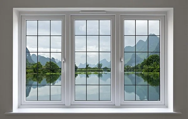 View through a three-pane window showing a lake, trees, and mountains under a cloudy sky.