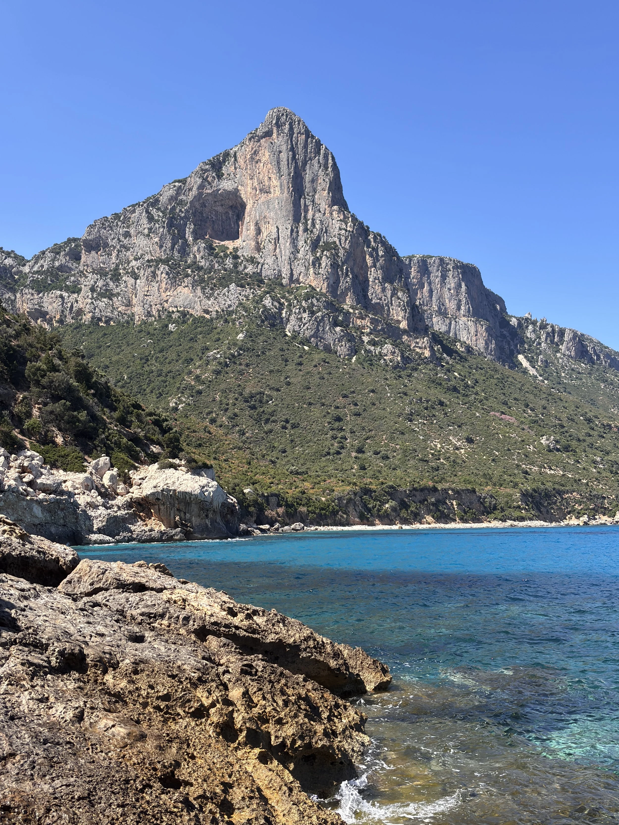 Berg mit felsiger Spitze über klarem, blauem Wasser und felsigen Ufern an der Küste.