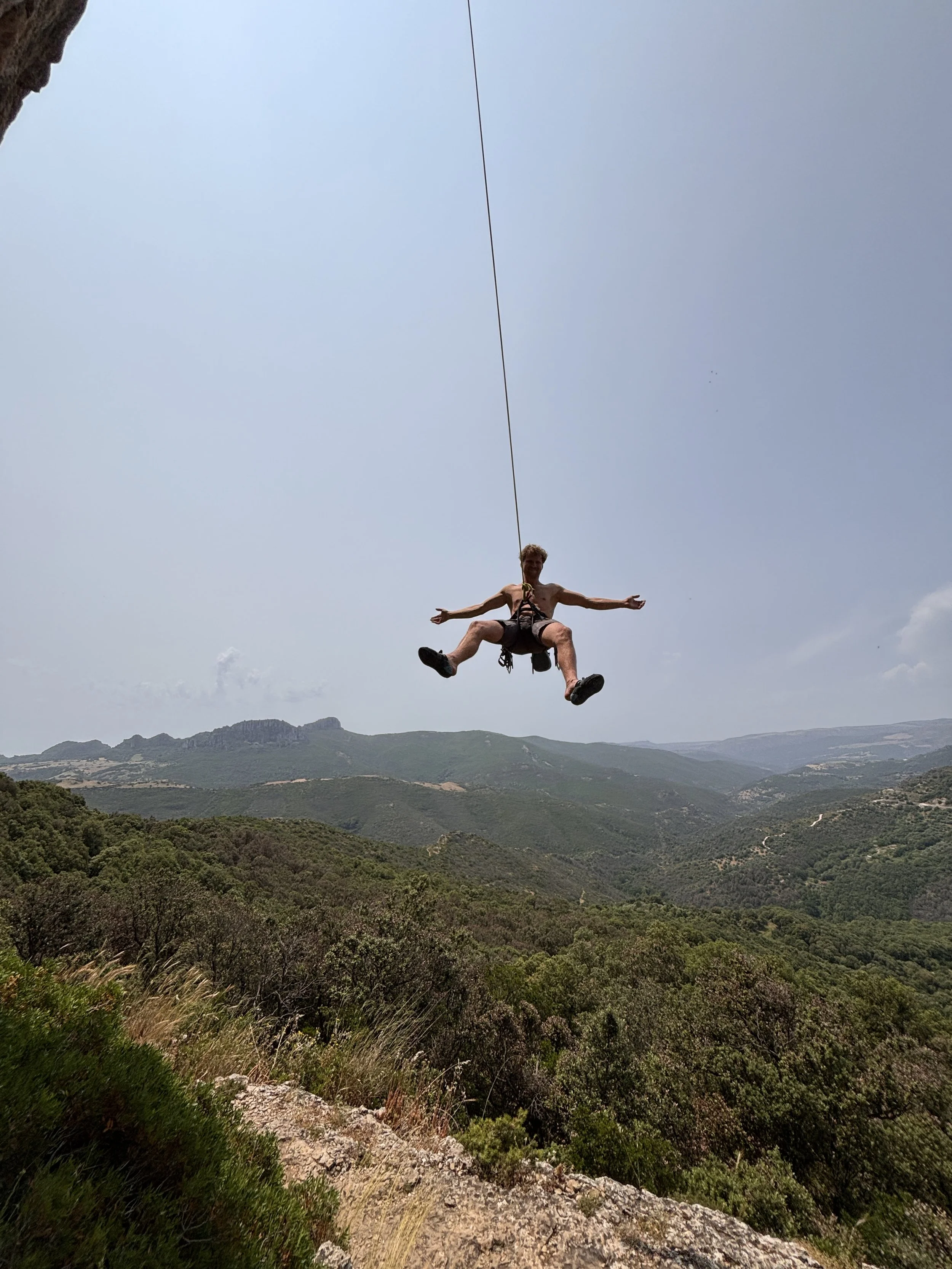 Junge Person schwingt an Seil über einer grünen Berglandschaft bei klarem Himmel.
