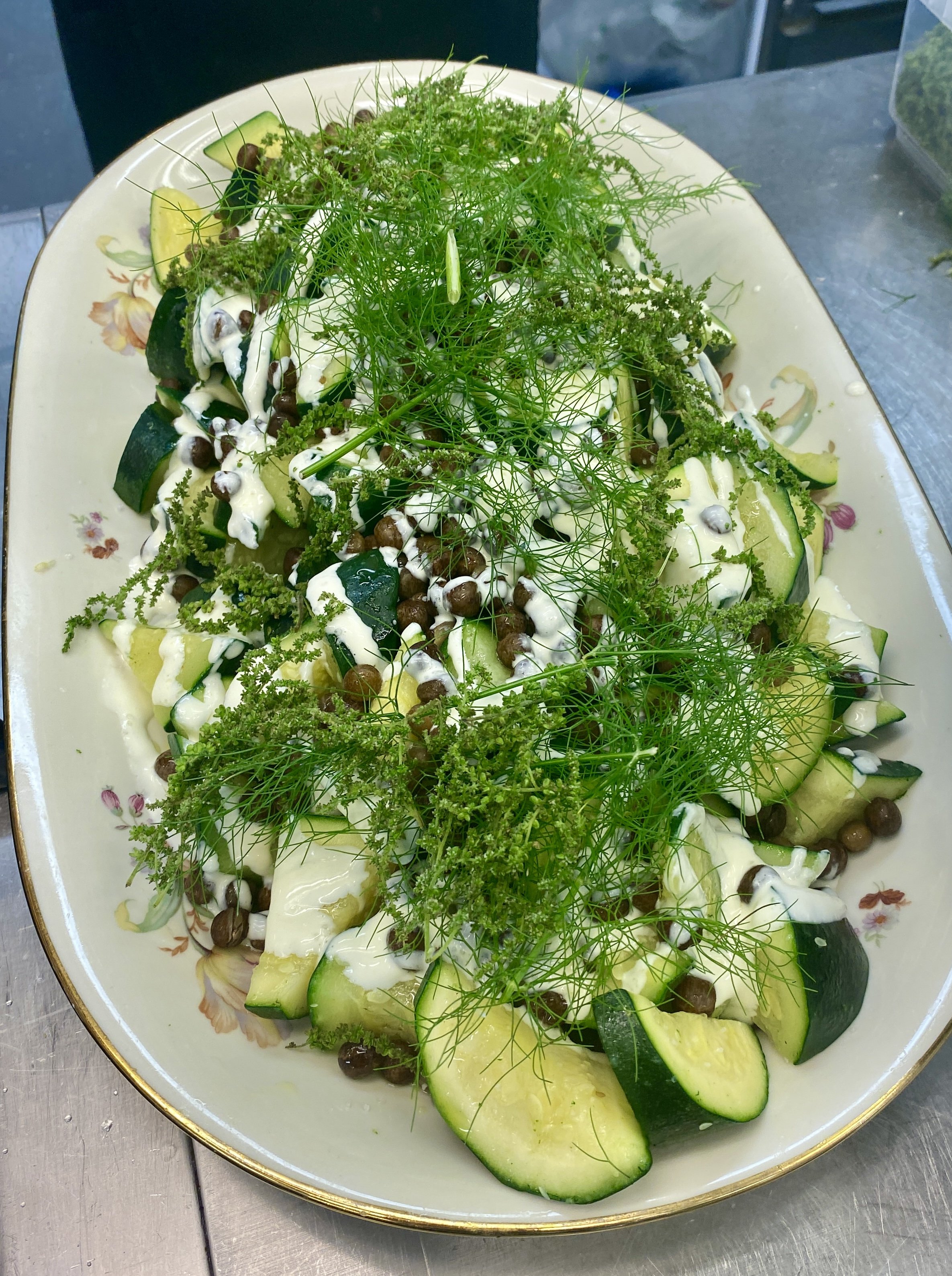 En salat squash, grønne urter, gråærter og yoghurt dressing, serveret i en dekorativ tallerken.