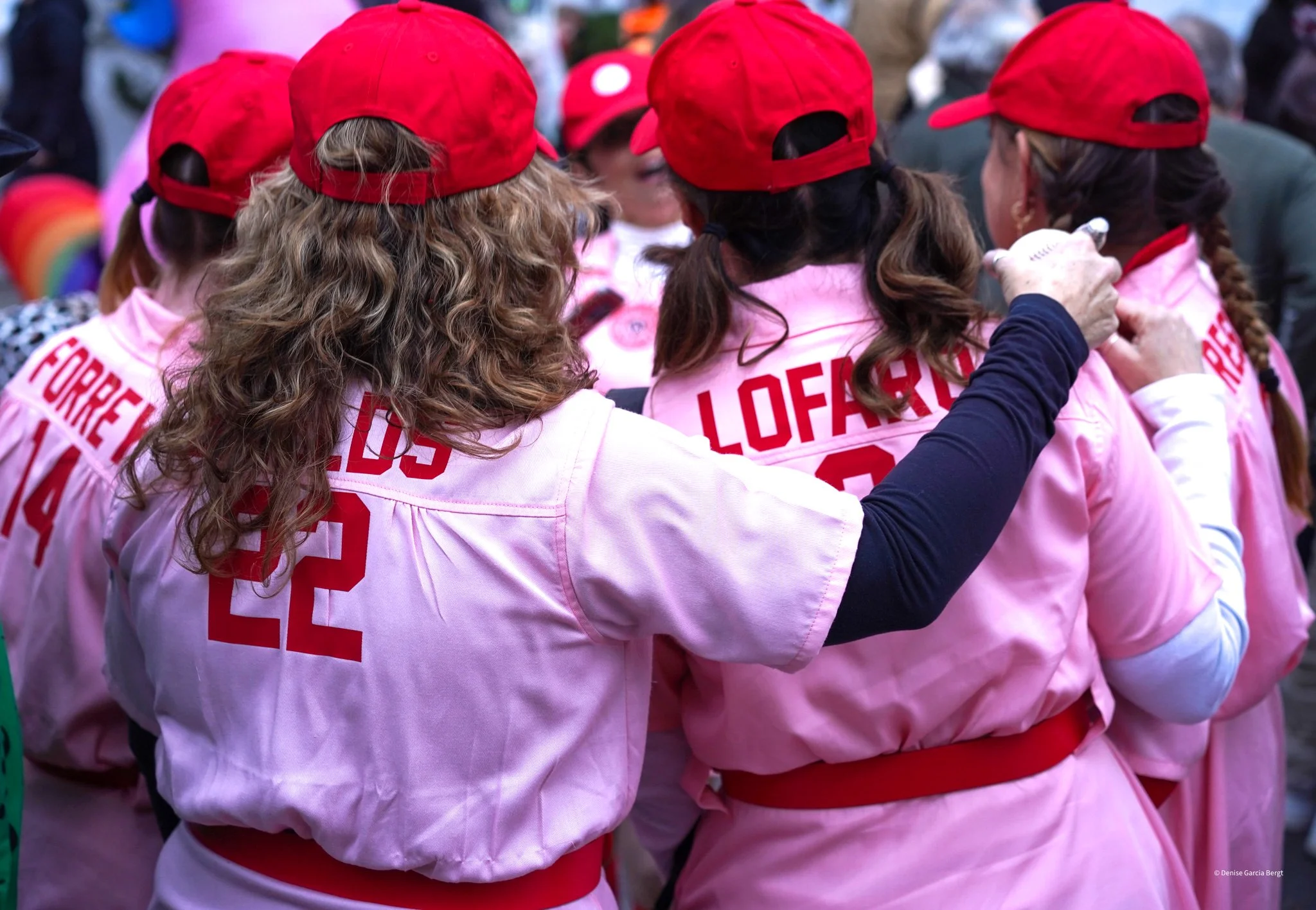 Group of women in pink uniforms and red caps, with one woman putting her hand on another's shoulder, during a gathering or event.