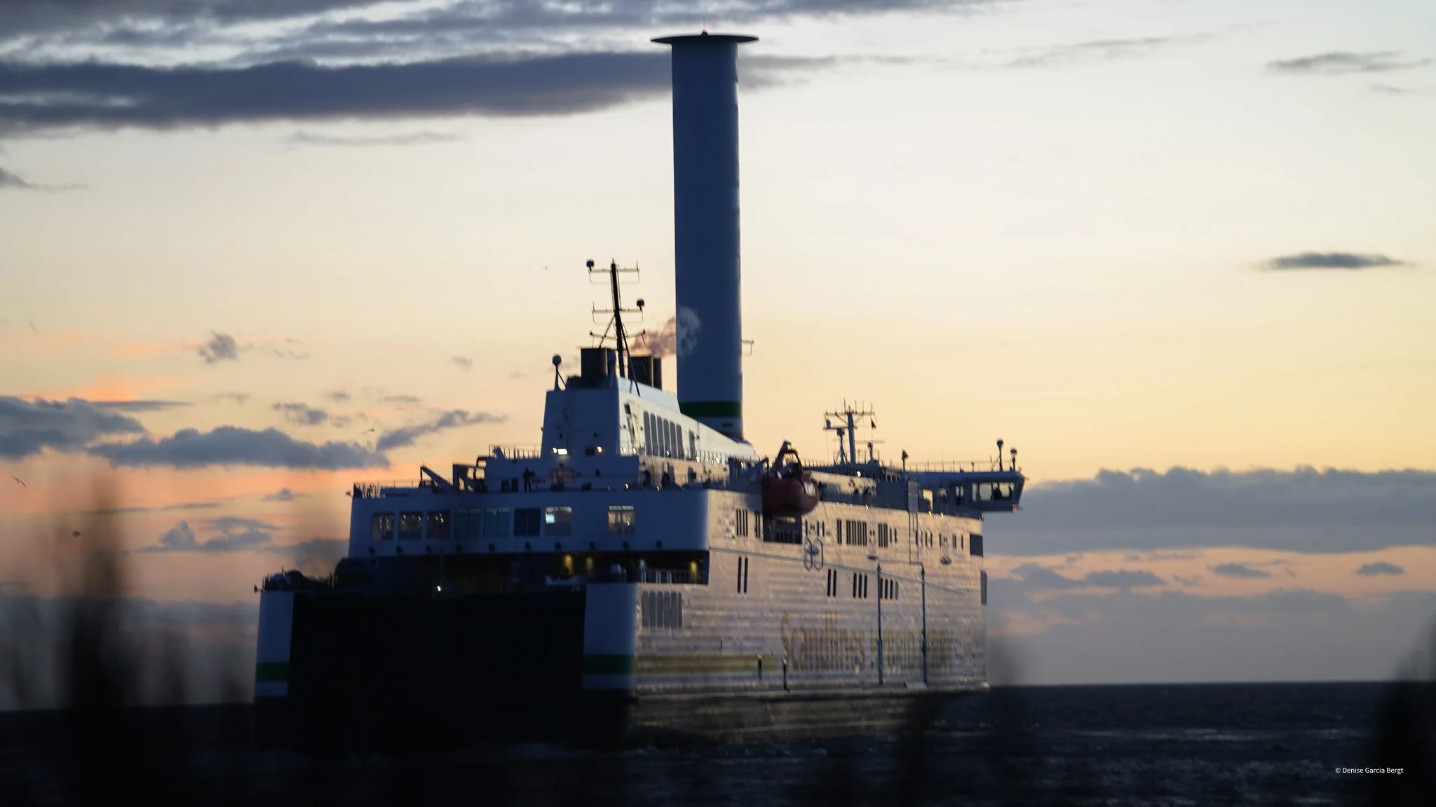 A ship with a large smokestack sailing against a sunset sky with clouds.