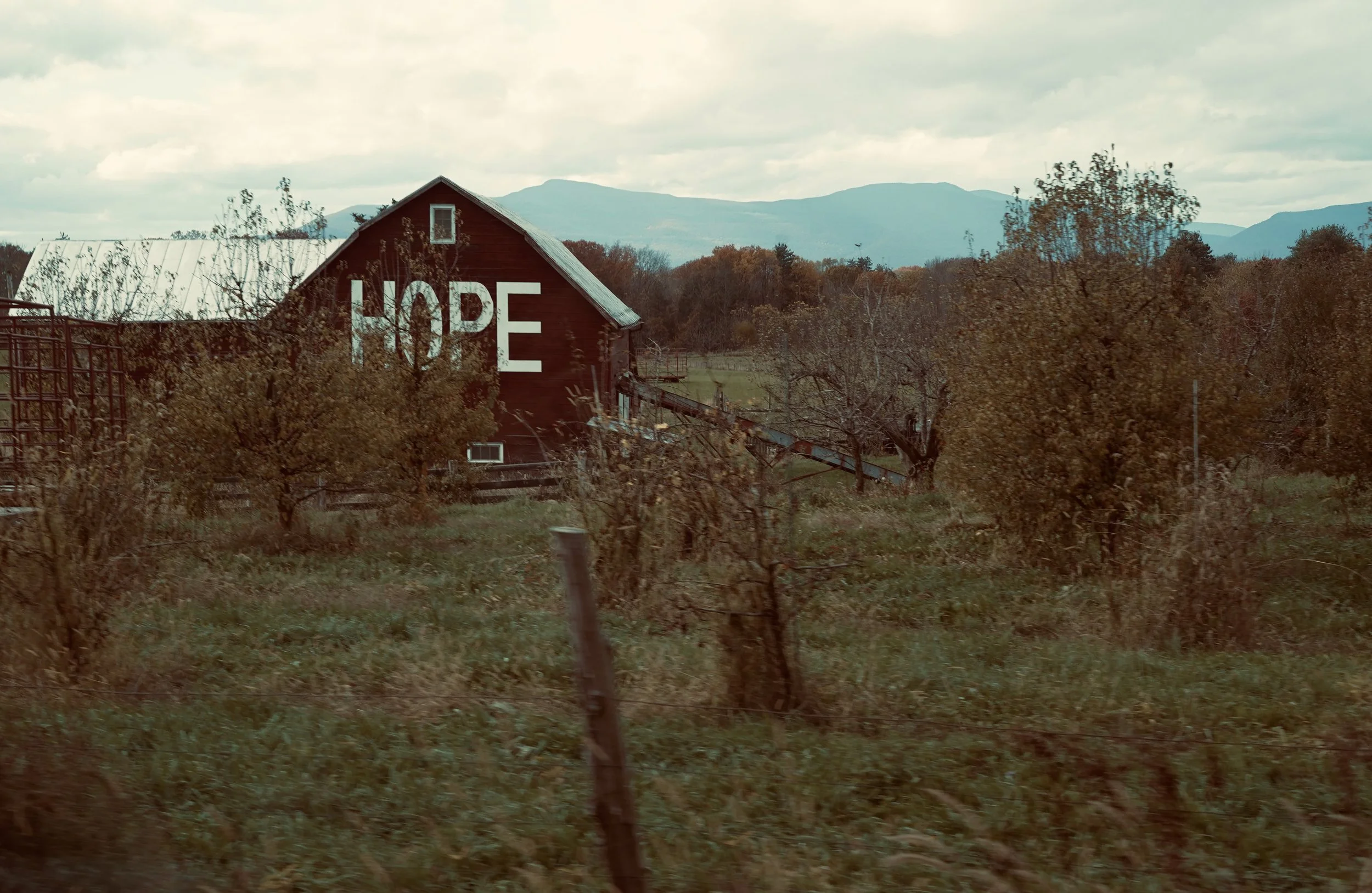 A rural scene with a red barn, which has the word 'HOPE' painted on it, surrounded by trees and mountains in the background.