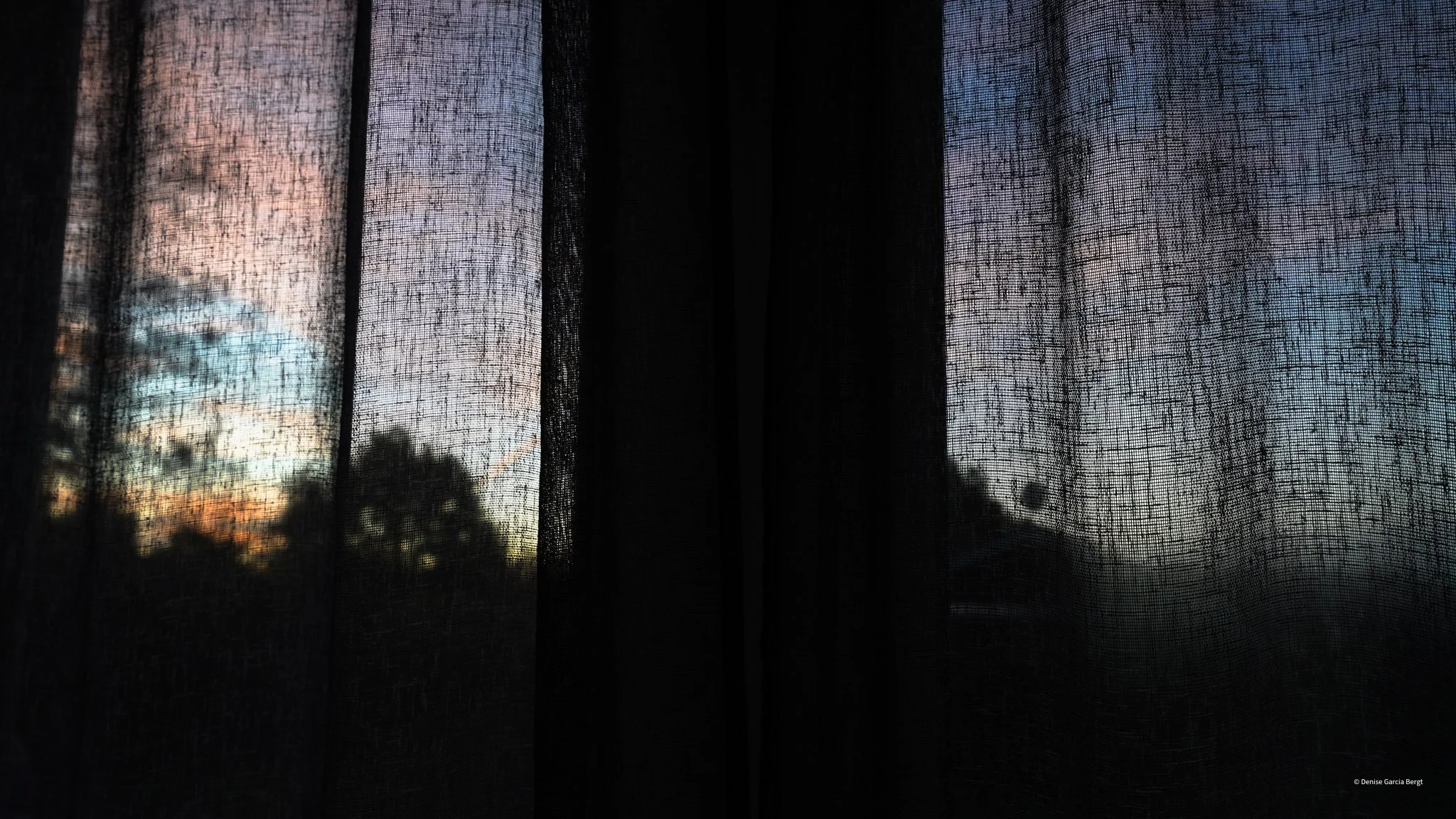 View of a sunset or sunrise through a semi-transparent curtain with trees visible in the background