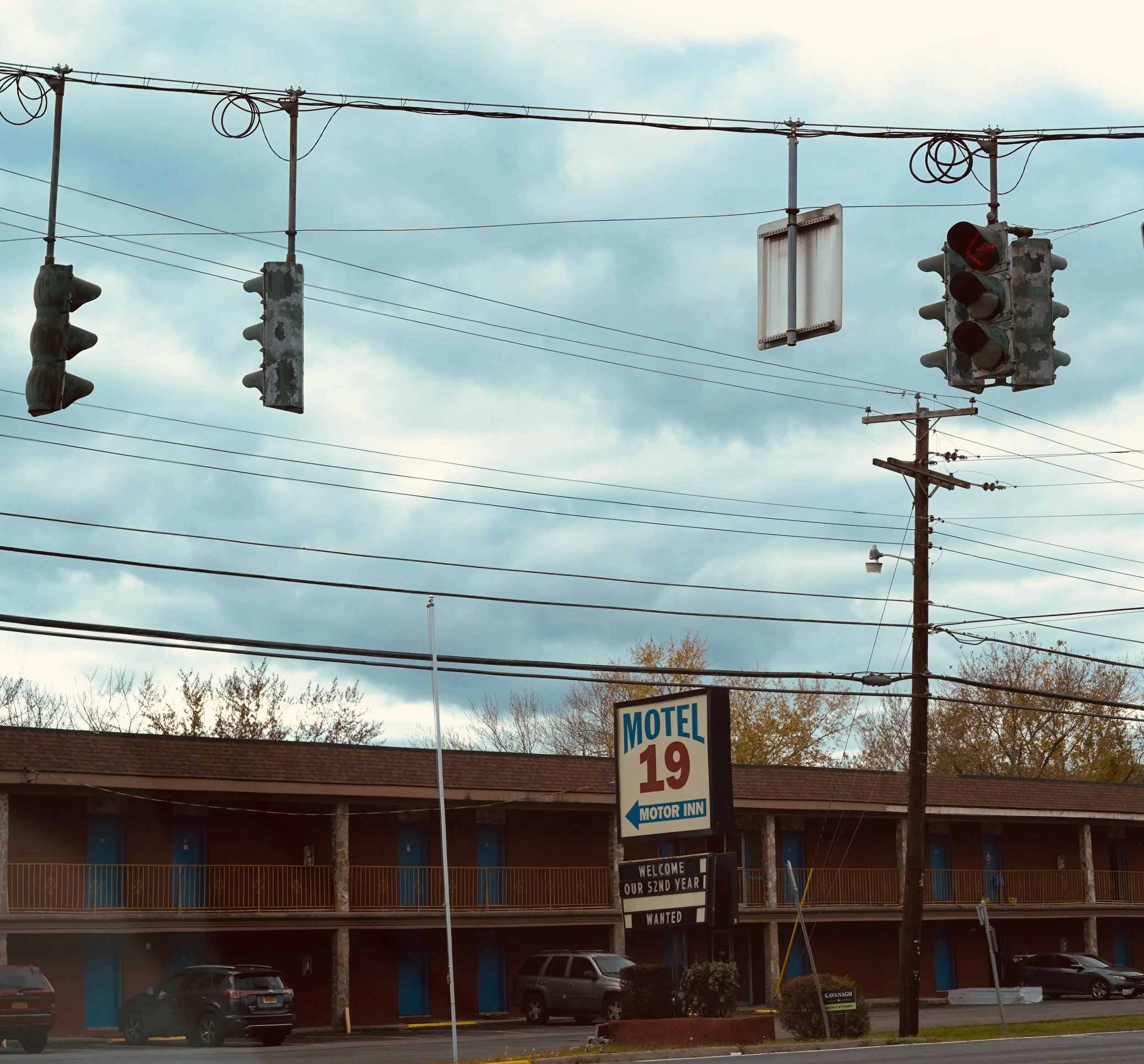 Street view with traffic lights, a motel sign advertising Motel 19 and Motor Inn, and parking lot with cars.
