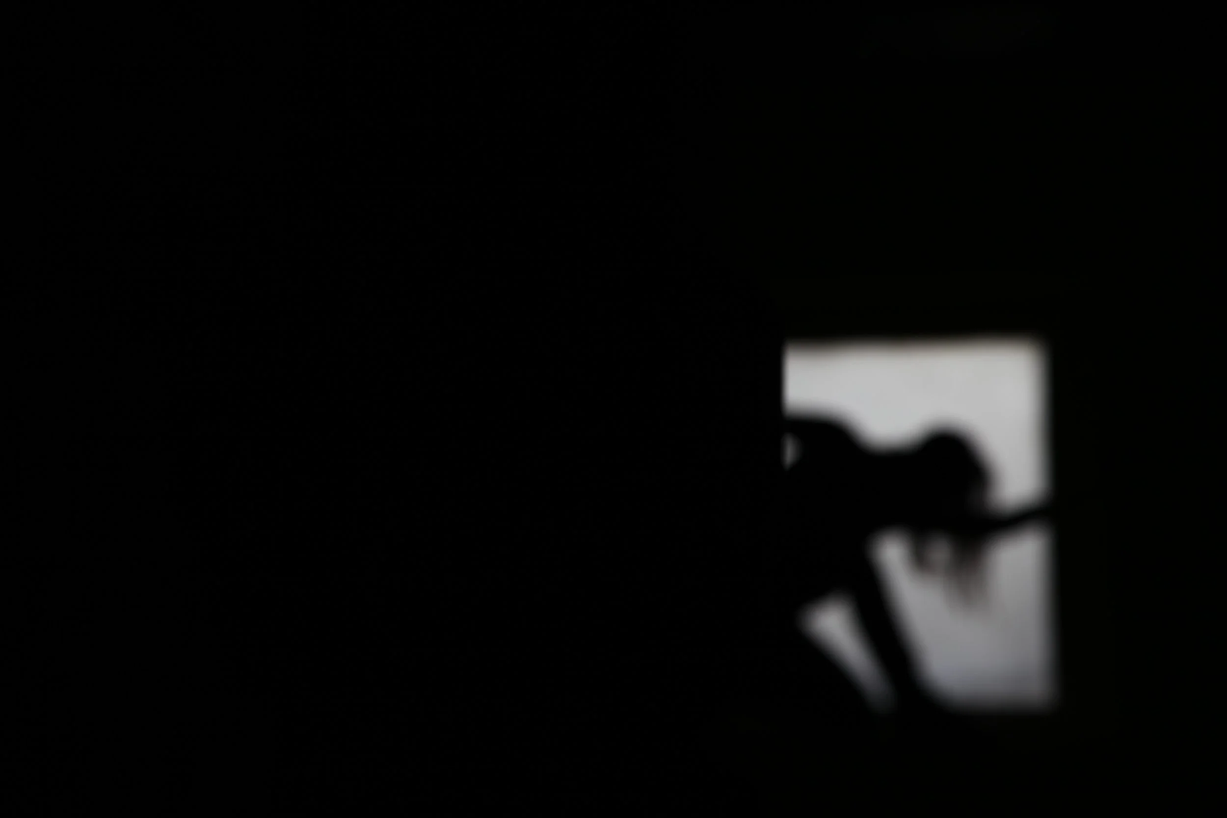 Silhouette of a person using a laptop in a dark room, with a faint light coming from a small screen or window.