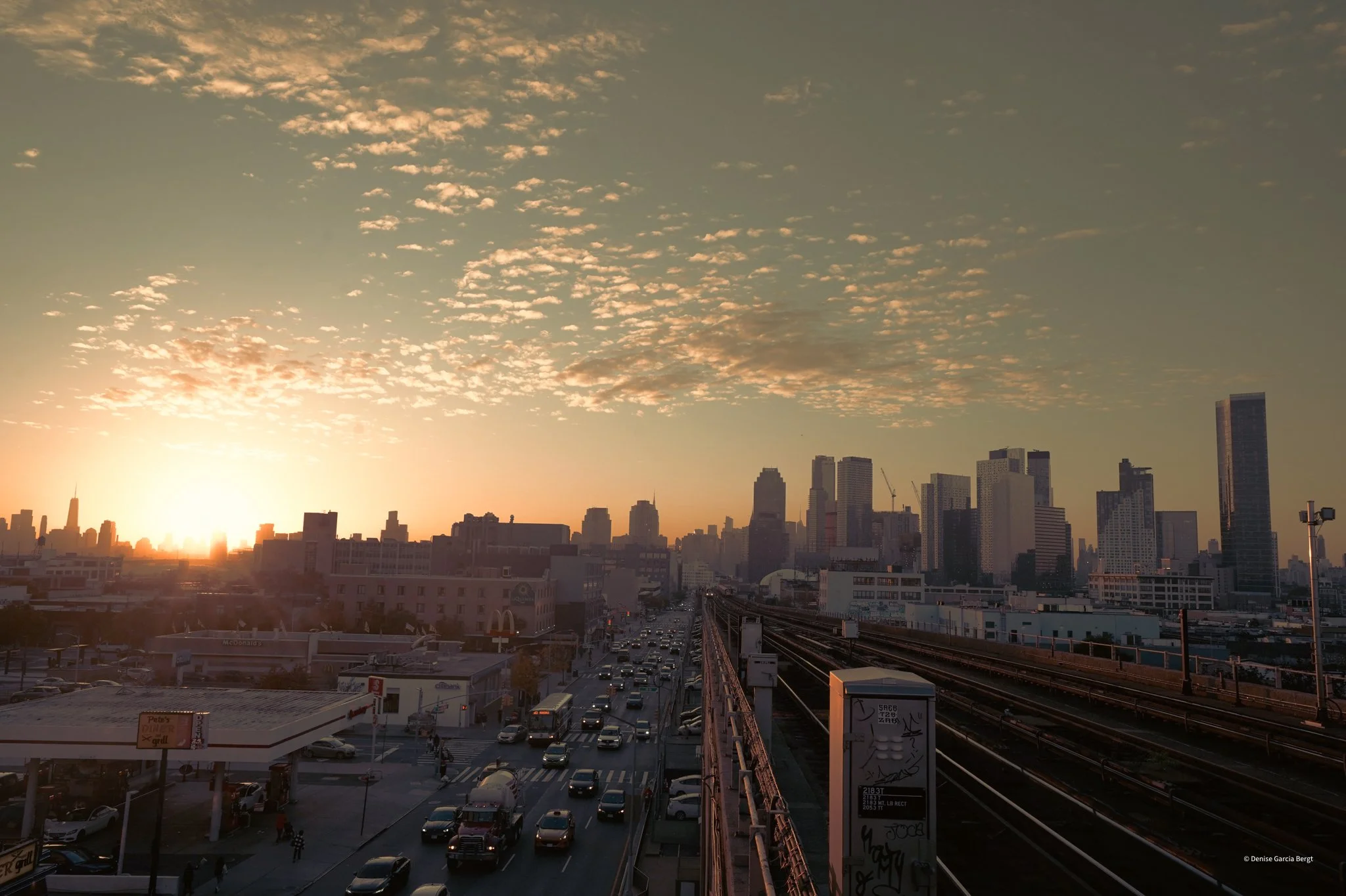Sunset over a city skyline with tall buildings, busy streets, and rail tracks.