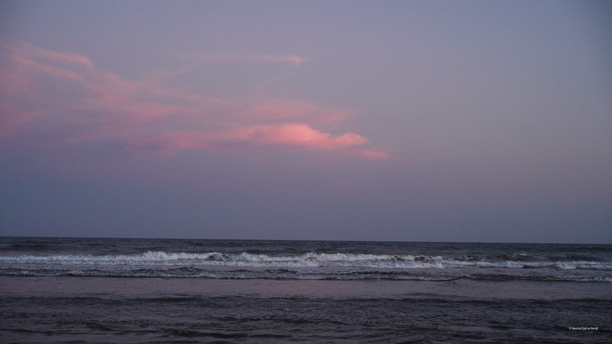 A view of the ocean at dusk with pink and purple clouds in the sky.