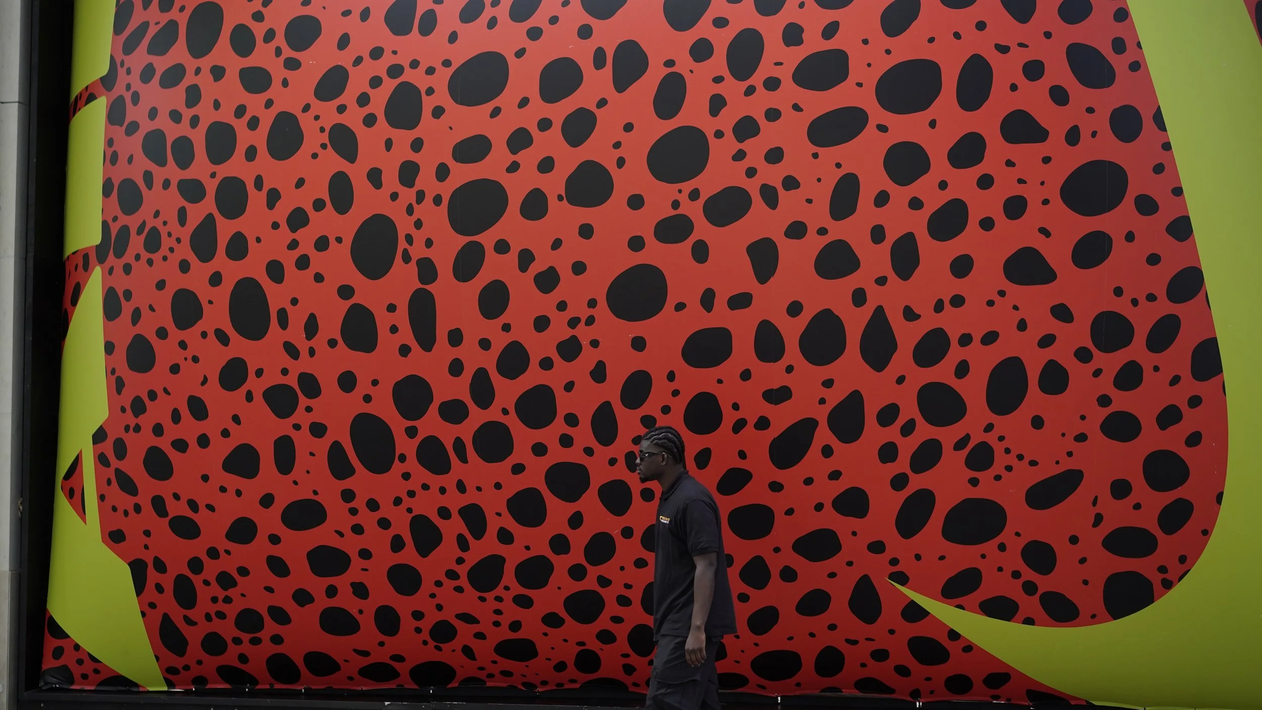 A man walking in front of a large wall with a leopard print design in red, black, and yellow-green.