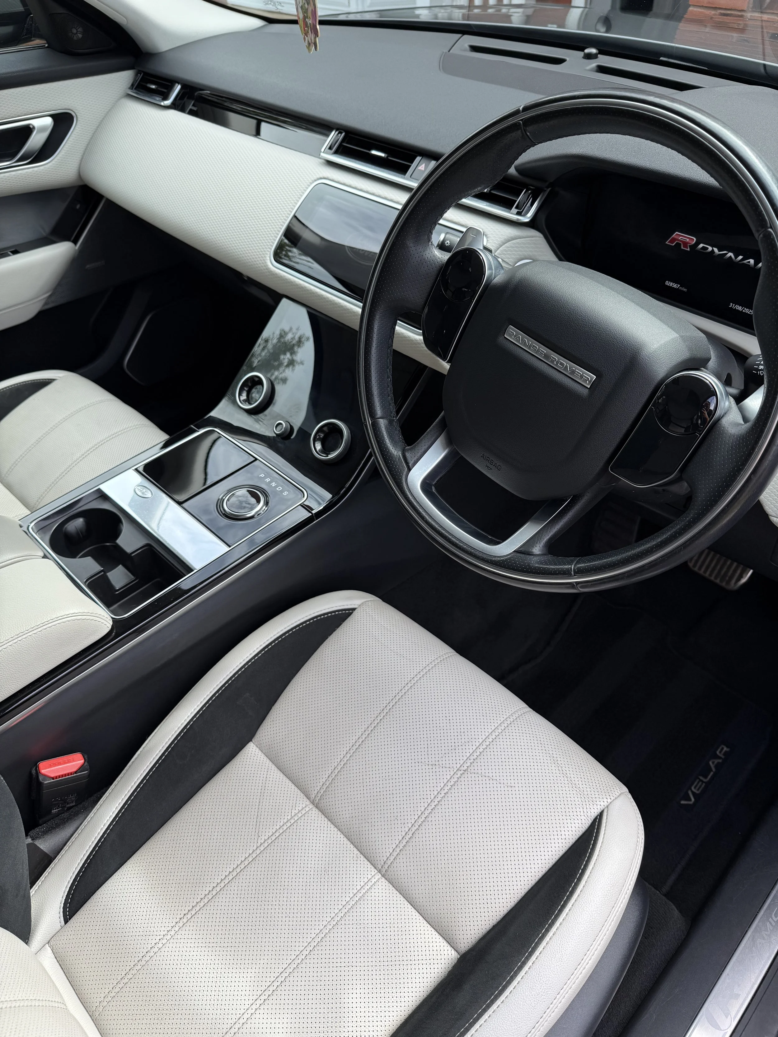 Interior of a Range Rover vehicle with a black dashboard, white leather seats, and a central console with a rotary gear selector.