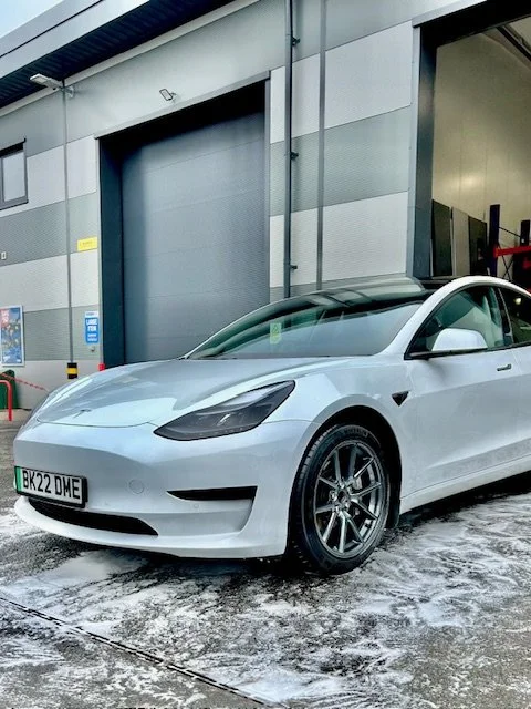 White Tesla Model 3 parked outside a building with snow on the ground.