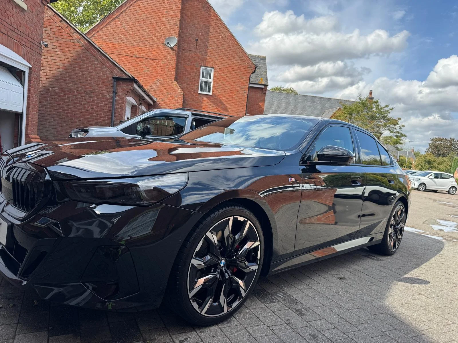 A shiny black BMW sedan parked outdoors in front of red brick houses under a partly cloudy sky.